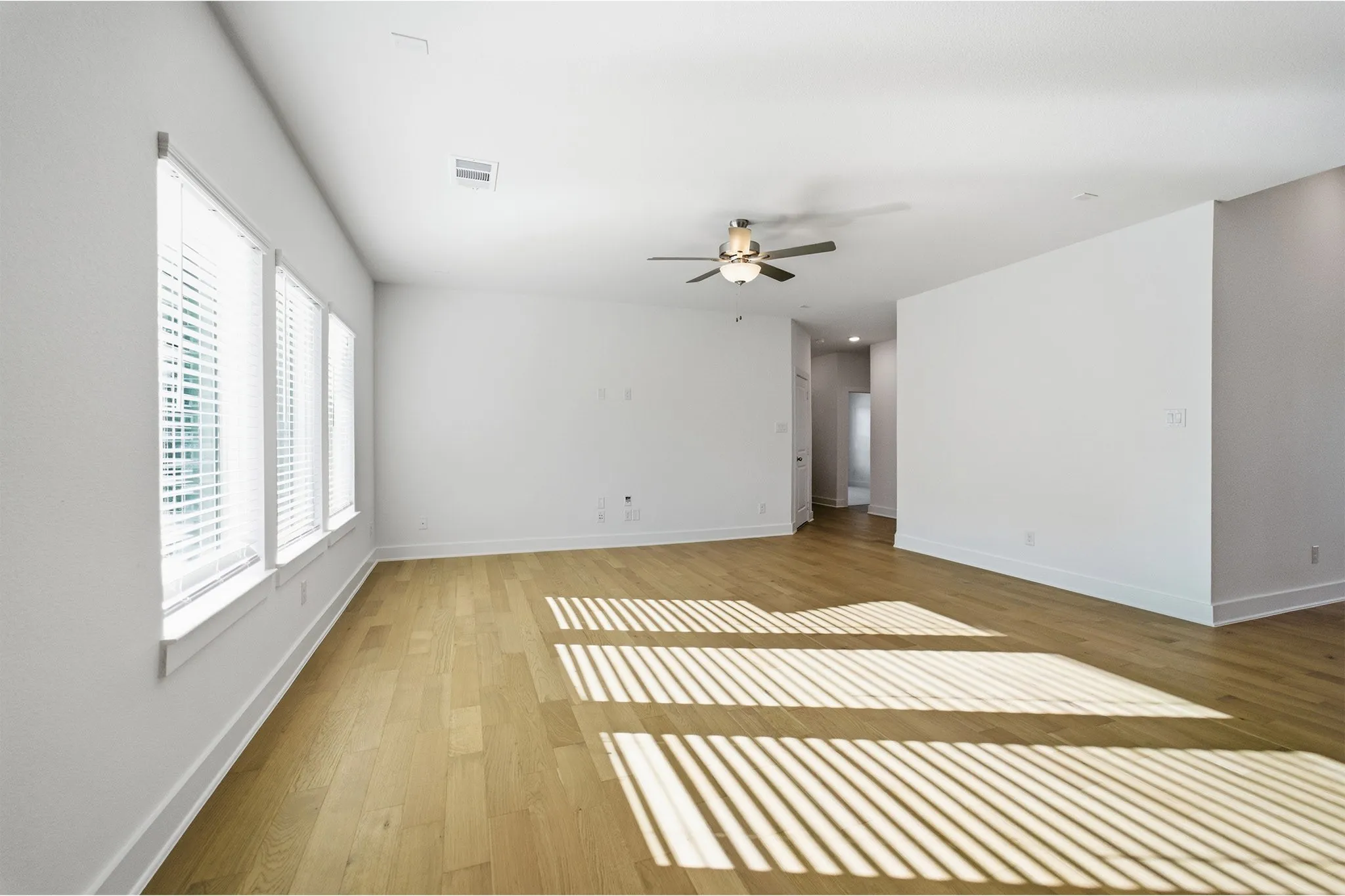 Spacious interior featuring light wood-finish flooring, multiple windows with blinds, a ceiling fan with integrated lighting, and neutral wall tones