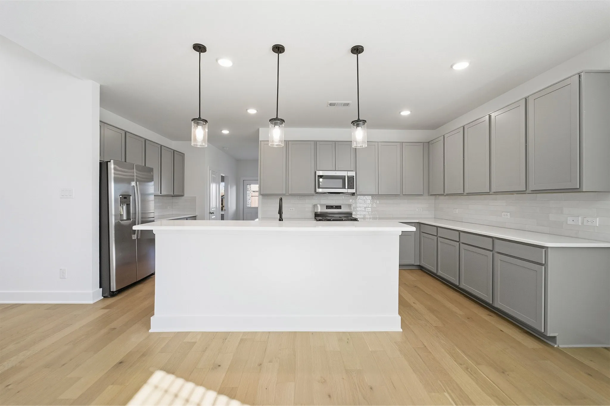 Kitchen featuring a central island, grey cabinetry, stainless steel appliances, light countertops, and wood-finish flooring