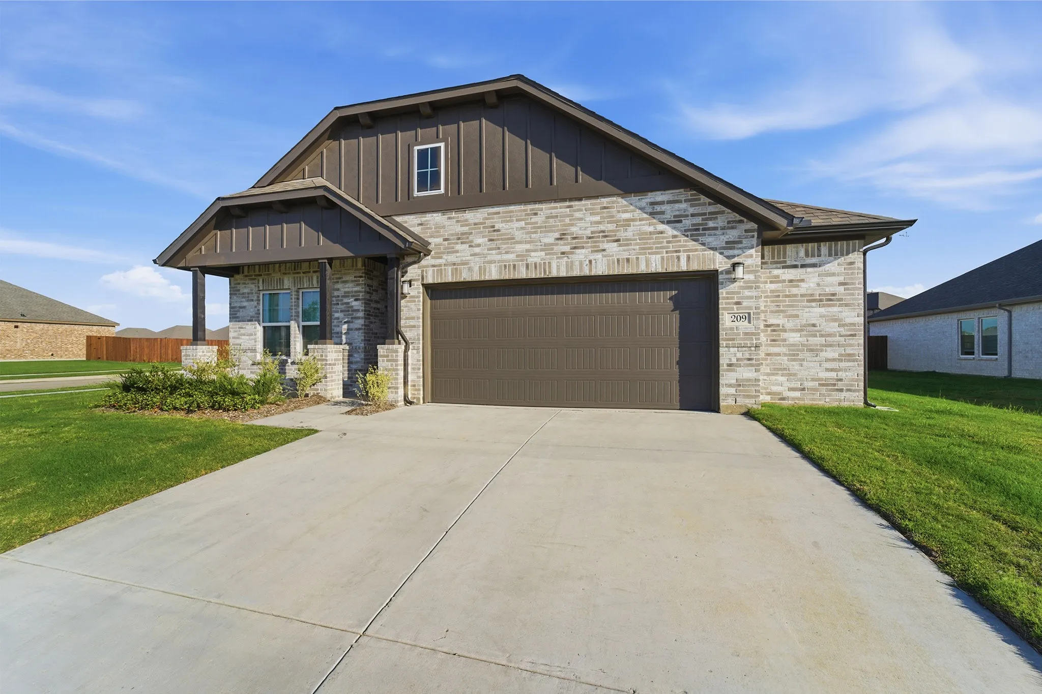 Brick and board-and-batten exterior featuring a covered entry porch, an integrated two-car garage, and a concrete driveway