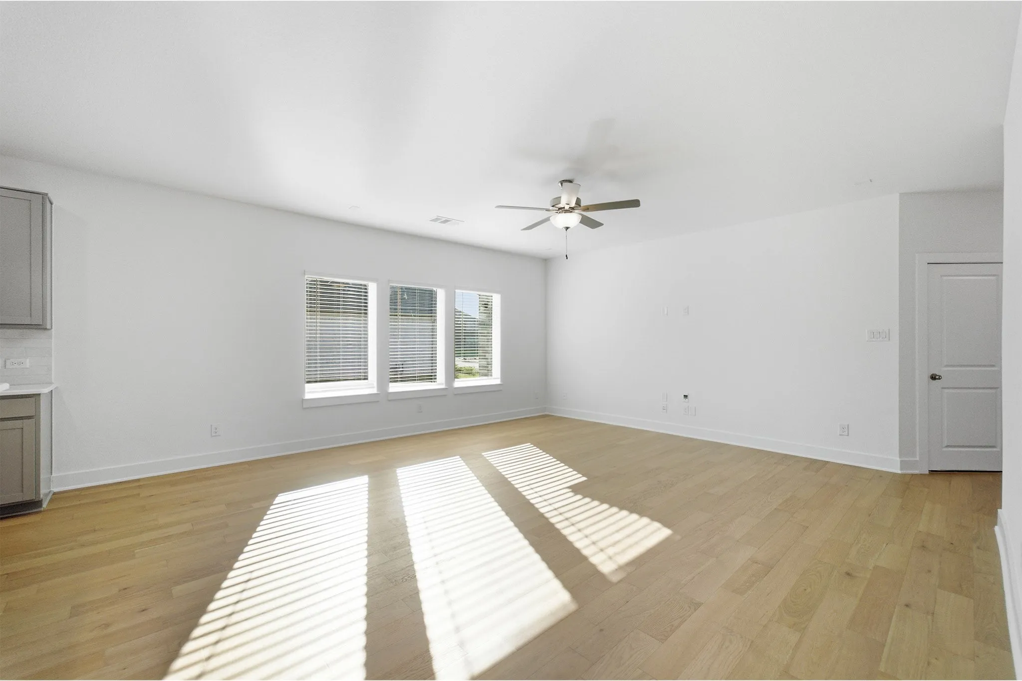 Spacious interior featuring light wood-finish flooring, white walls, and a ceiling fan with integrated lighting