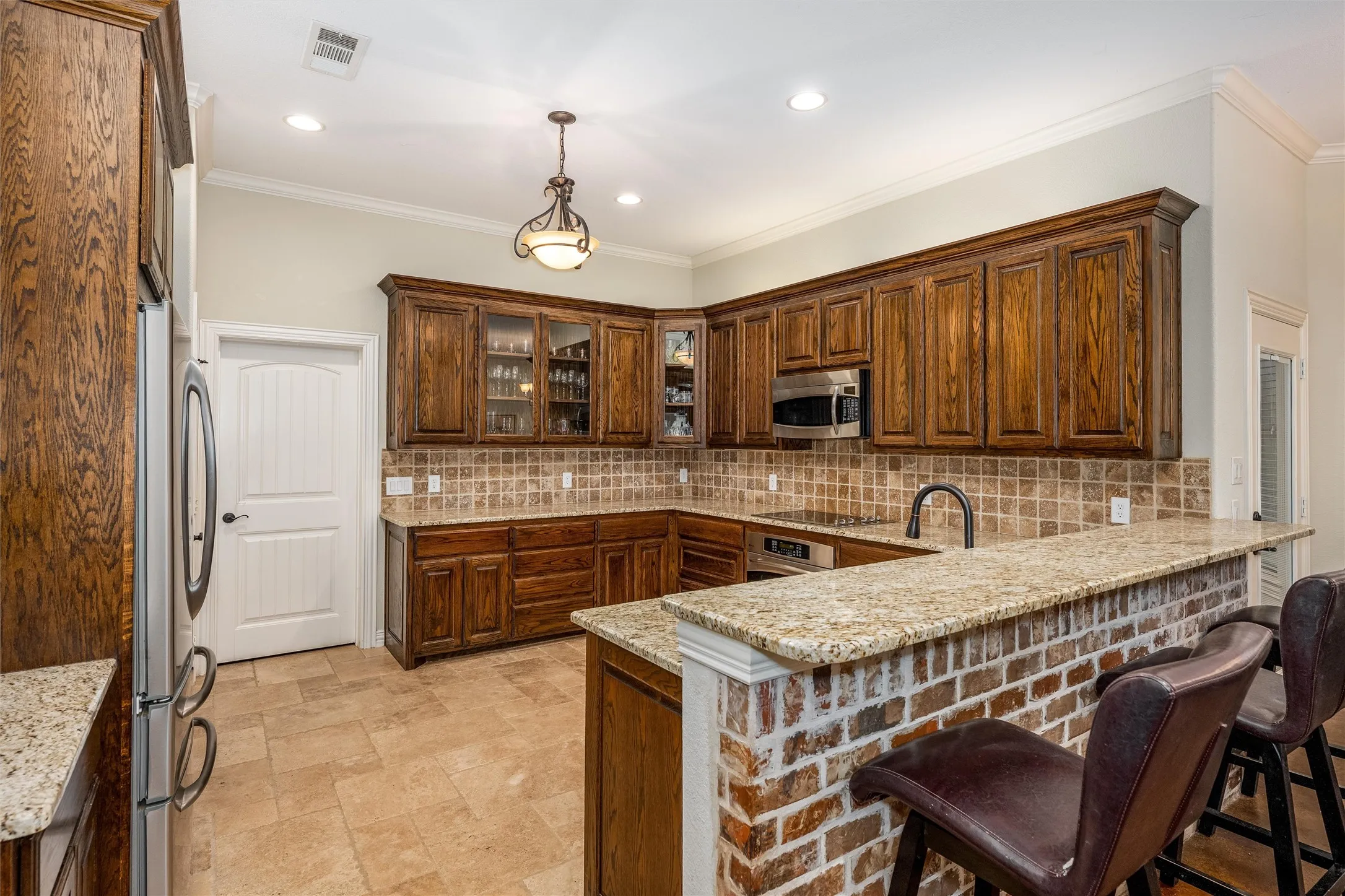 Kitchen featuring decorative light fixtures, granite countertops, glass insert cabinets, and appliances with stainless steel finishes