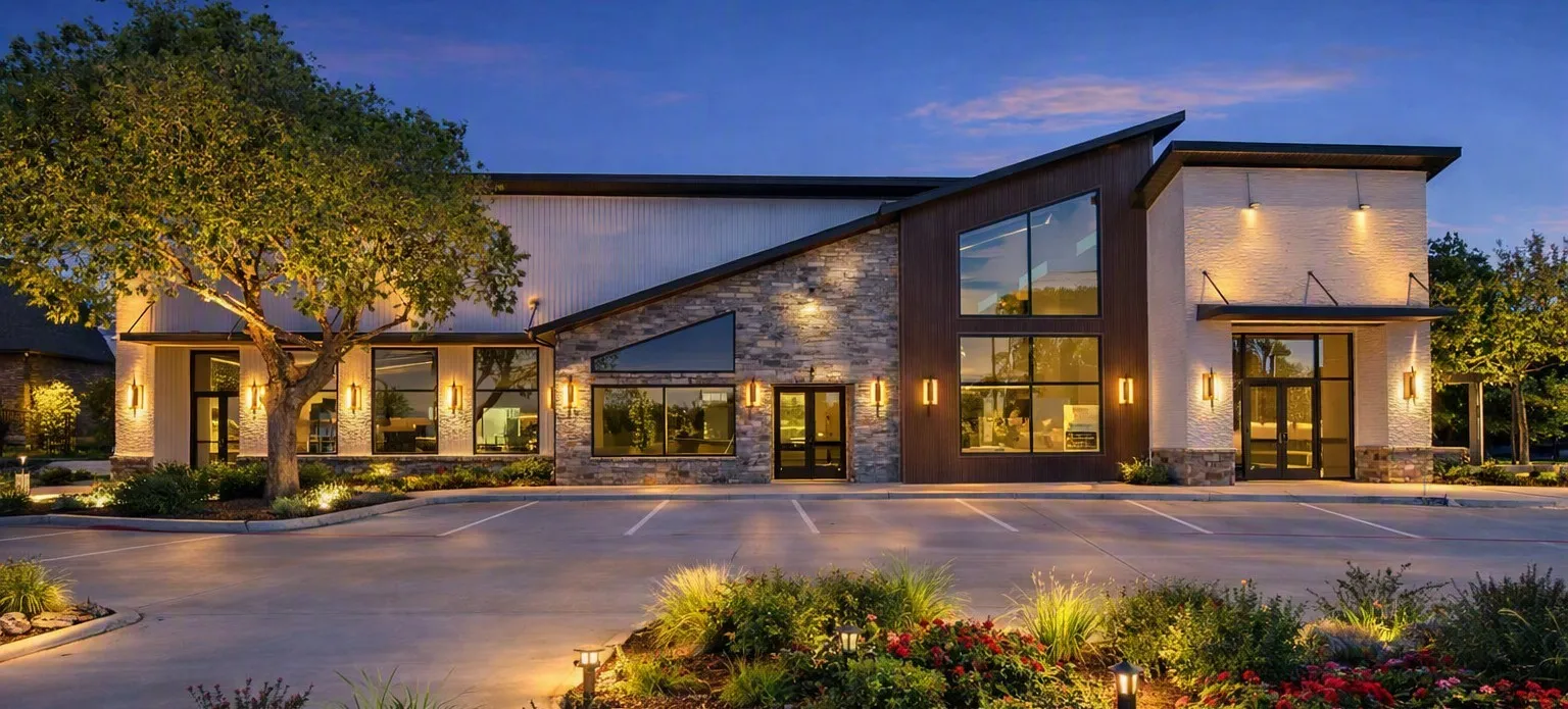 Contemporary exterior with stone and wood-finish accents, expansive windows, multiple entryways, a paved parking area, and manicured landscaping