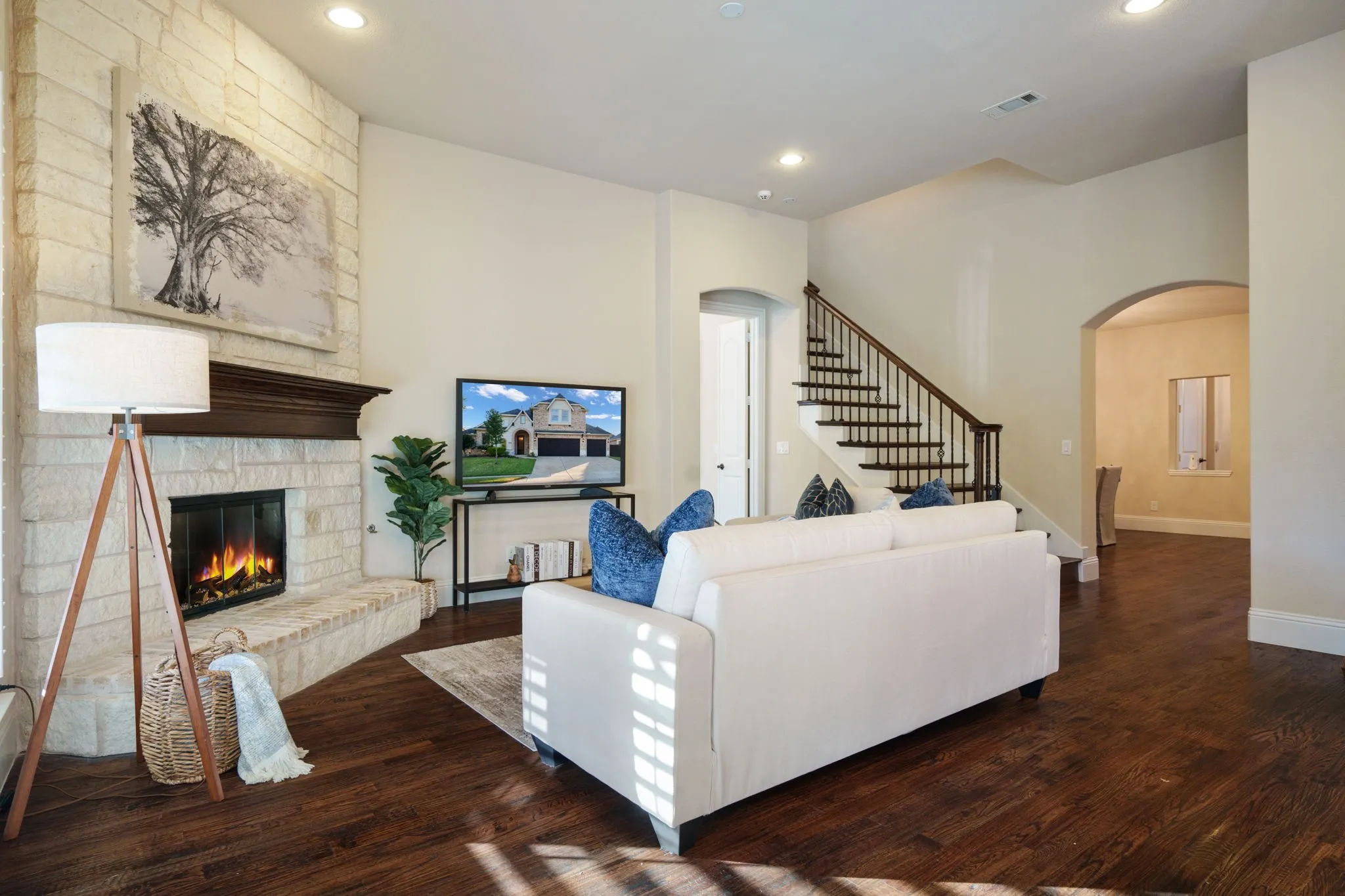 Warm and open living area with wood floors, cozy fireplace, and staircase leading to the upstairs game room.