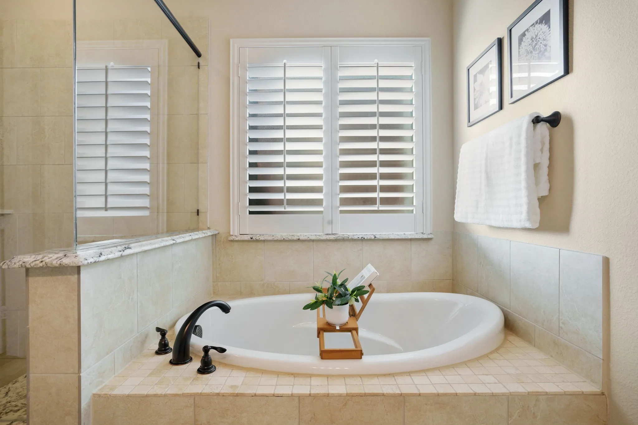 Luxurious soaking tub with granite accents, tile surround, and plantation shutters for privacy and light.