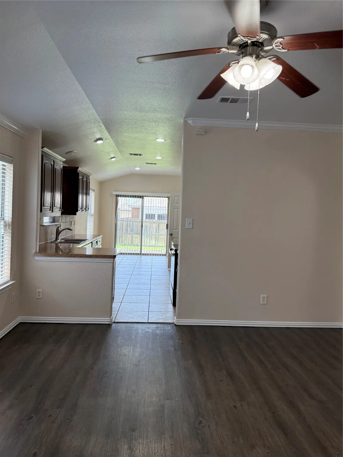 Unfurnished living room with vaulted ceiling, dark wood-style floors, a ceiling fan, crown molding, and a textured ceiling