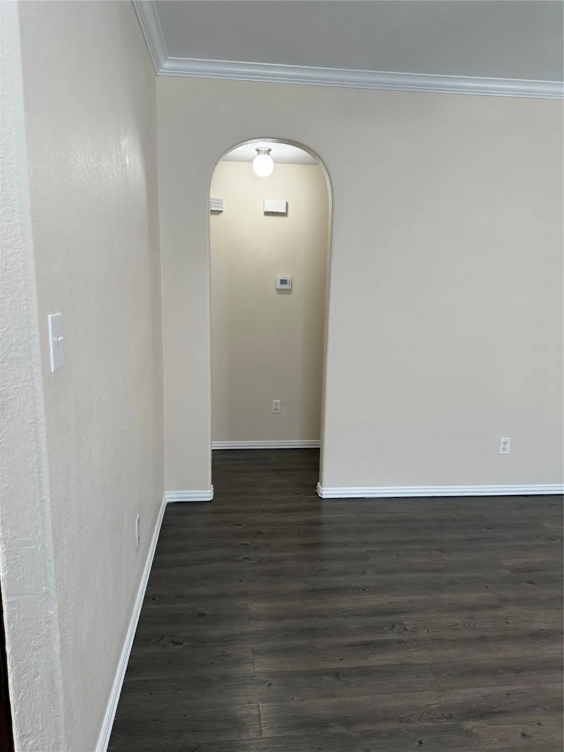 Unfurnished room with arched walkways, dark wood-type flooring, and ornamental molding