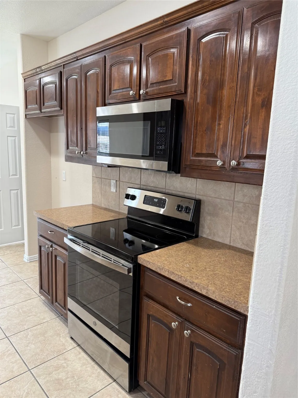 Kitchen featuring stainless steel range oven, dark brown cabinets, backsplash, and light tile patterned floors