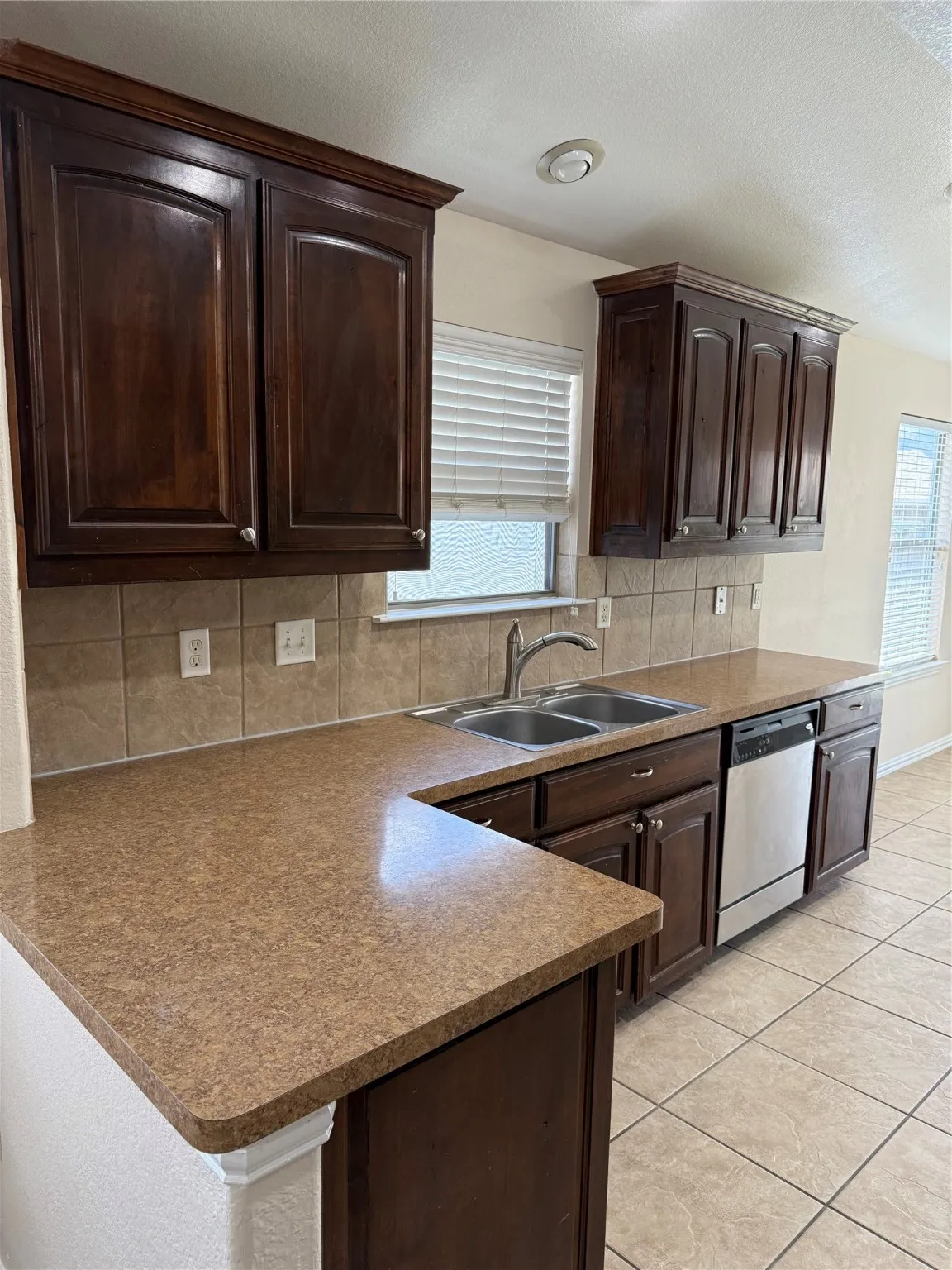 Kitchen featuring dark brown cabinetry, a peninsula, a textured ceiling, decorative backsplash, and dishwasher