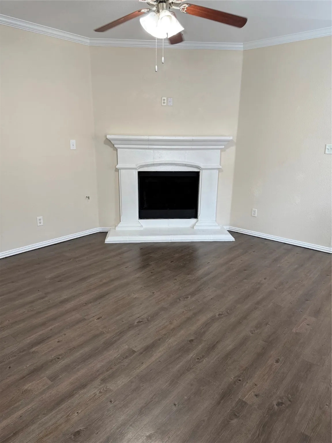 Unfurnished living room with ornamental molding, a fireplace with raised hearth, dark wood-style flooring, and a ceiling fan