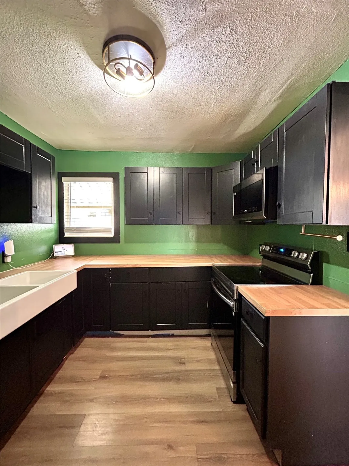 Kitchen with range with electric stovetop, a textured ceiling, light countertops, and light wood-style flooring