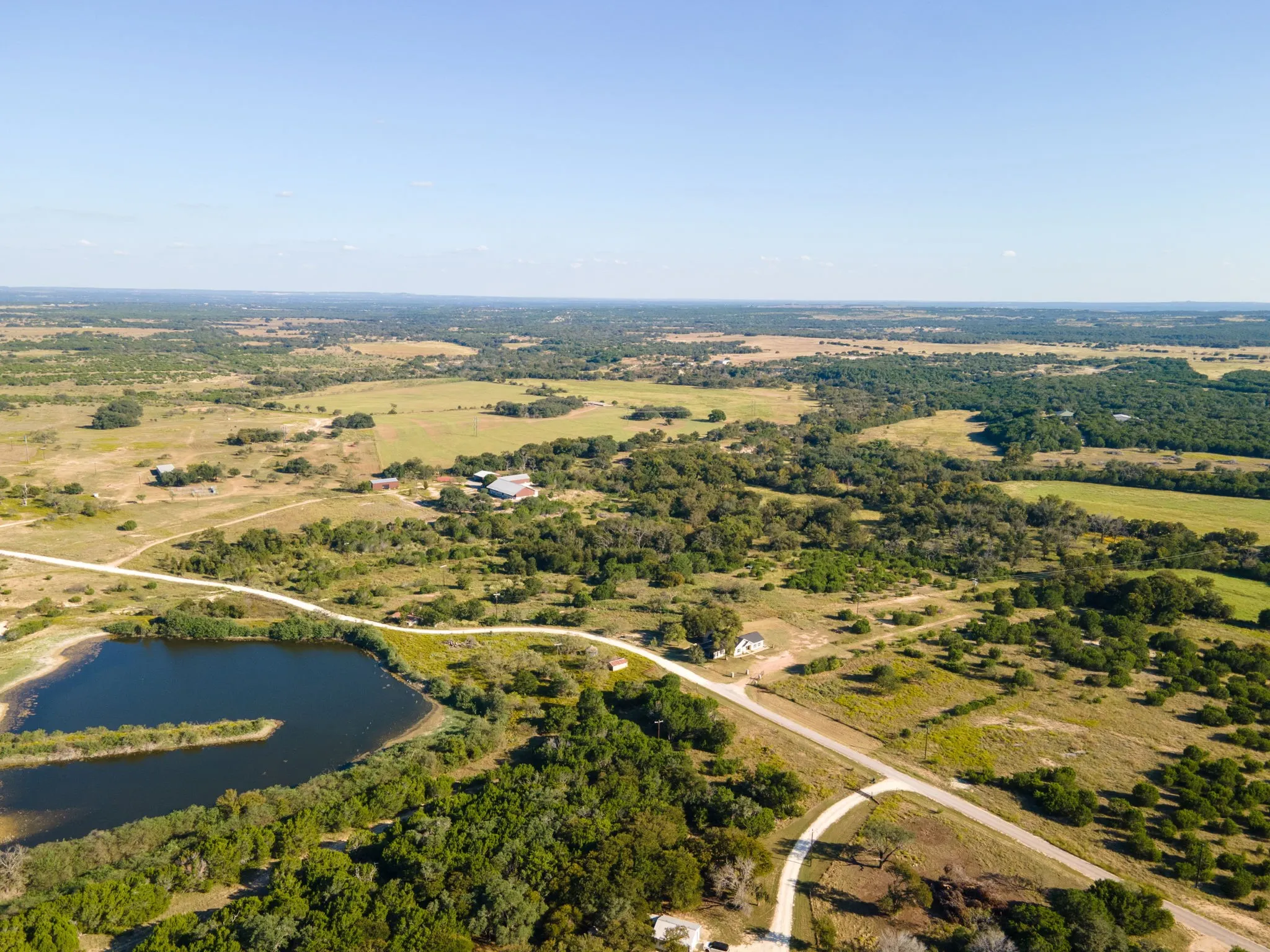 Expansive rural landscape featuring a private body of water, numerous mature trees, and open fields