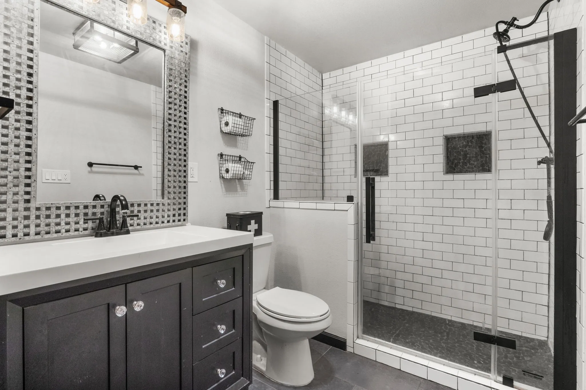 Modern bathroom featuring a dark wood-finish vanity with a light-toned countertop, a glass-enclosed shower with subway tile surround, a built-in shower niche, a rain shower head, and a decorative grid-pattern mirror