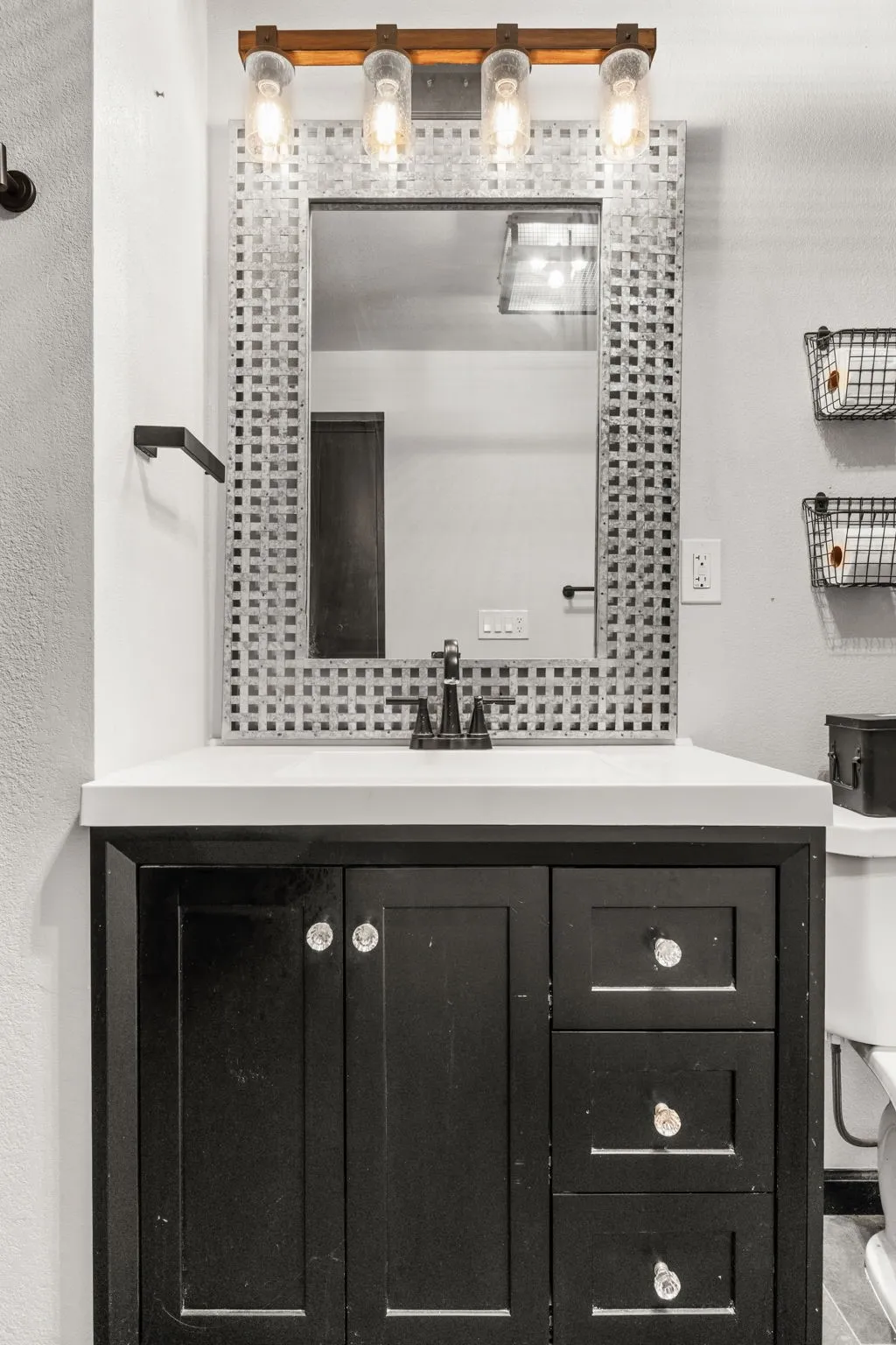 Bathroom vanity featuring a dark wood-finish cabinet with crystal knobs, a light-toned countertop, and a rectangular mirror with a textured frame