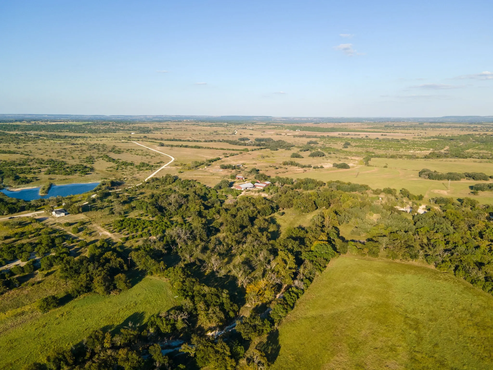 Expansive rural landscape featuring a private body of water, extensive tree coverage, and open grassy areas