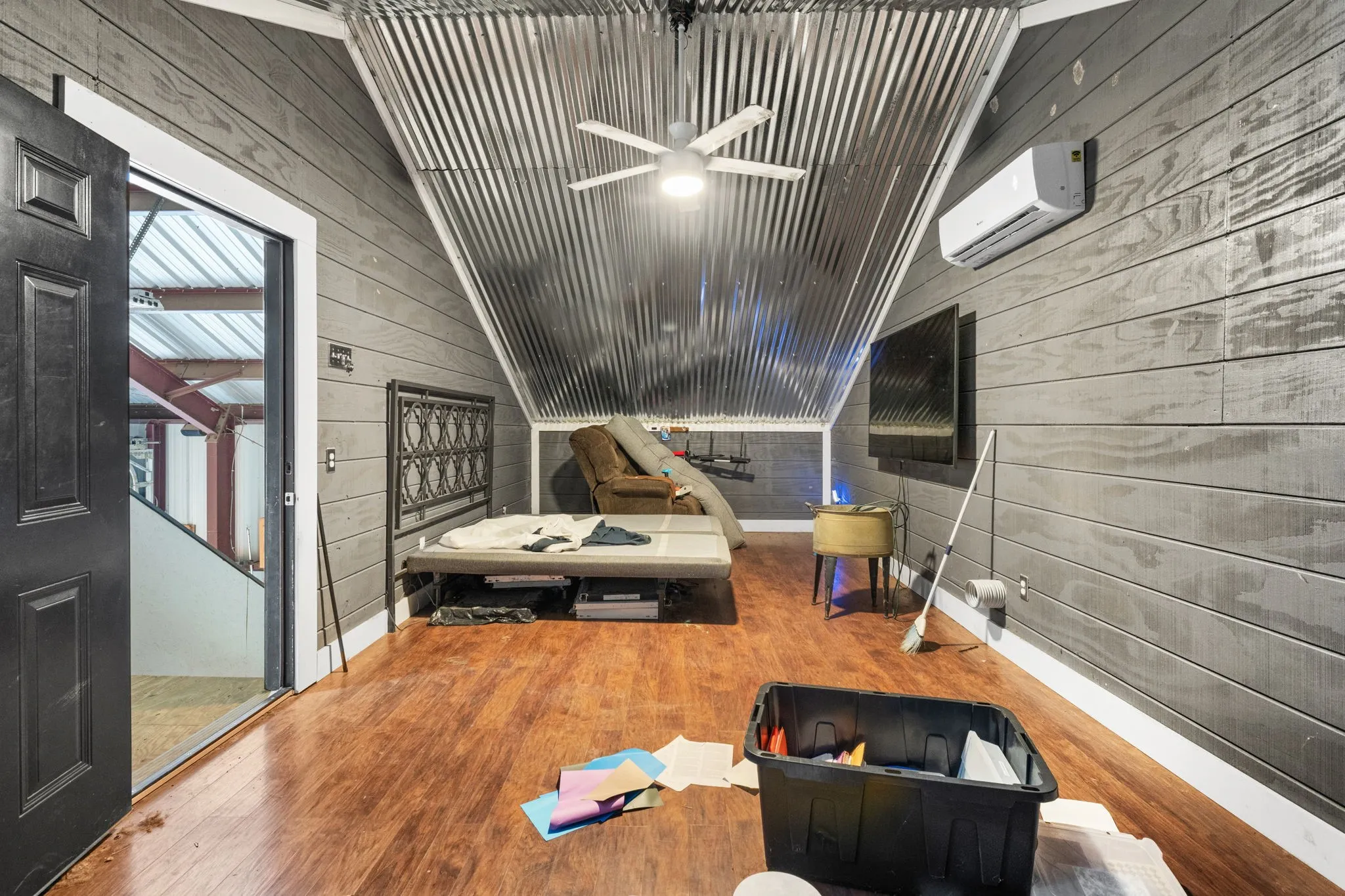 Room featuring wood-finish flooring, dark plank walls, and a corrugated metal ceiling