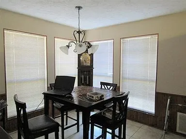 Dining area featuring a textured ceiling, a wainscoted wall, light tile patterned floors, wood walls, and a chandelier