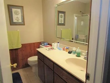 Bathroom with wooden walls, a wainscoted wall, a shower stall, vanity, and light tile patterned floors
