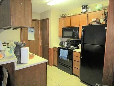 Kitchen with black appliances, light countertops, light tile patterned floors, brown cabinets, and a wainscoted wall