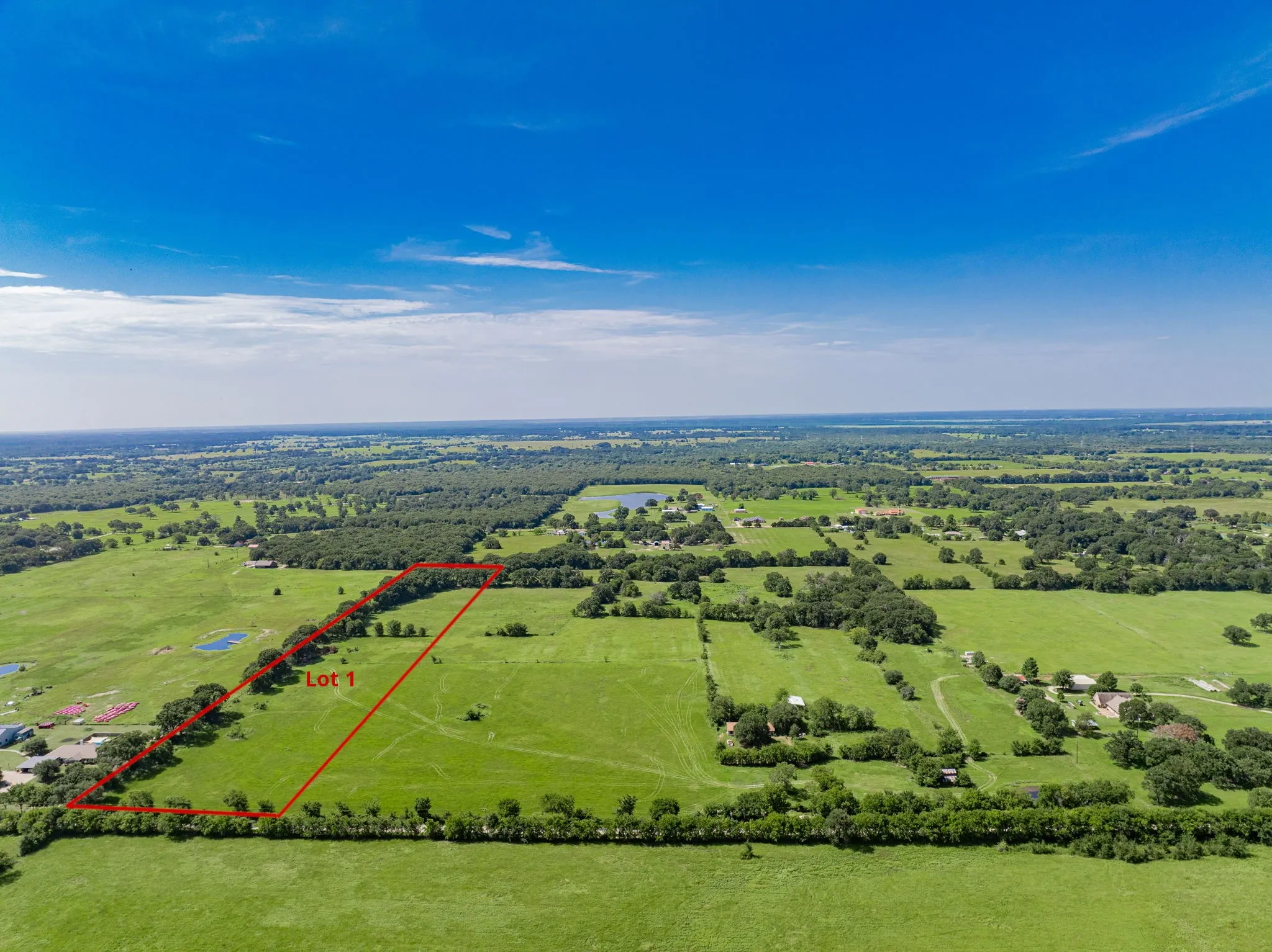Expansive green acreage featuring scattered trees and a clear blue sky overhead