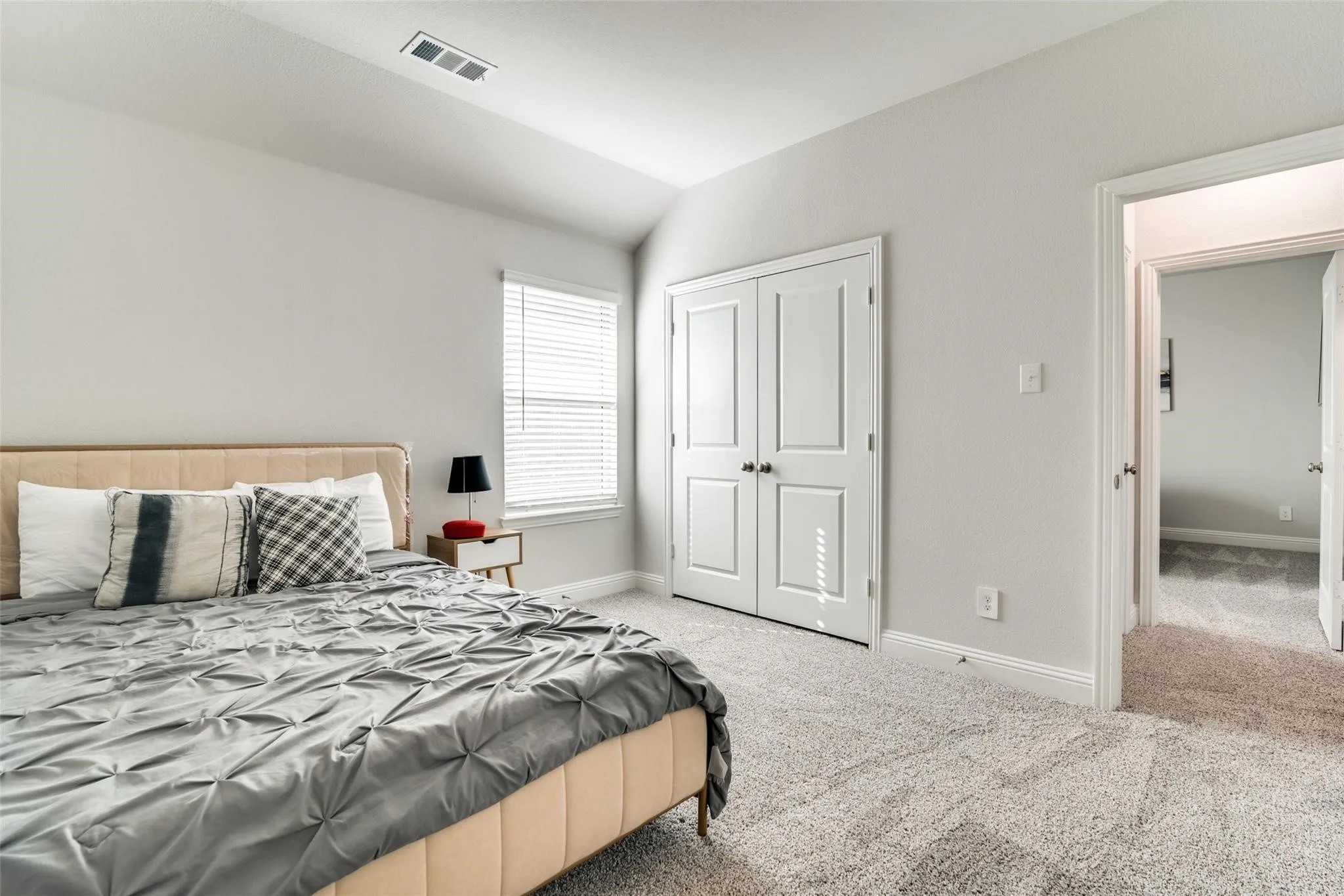 Bedroom with light colored carpet, vaulted ceiling, and a closet