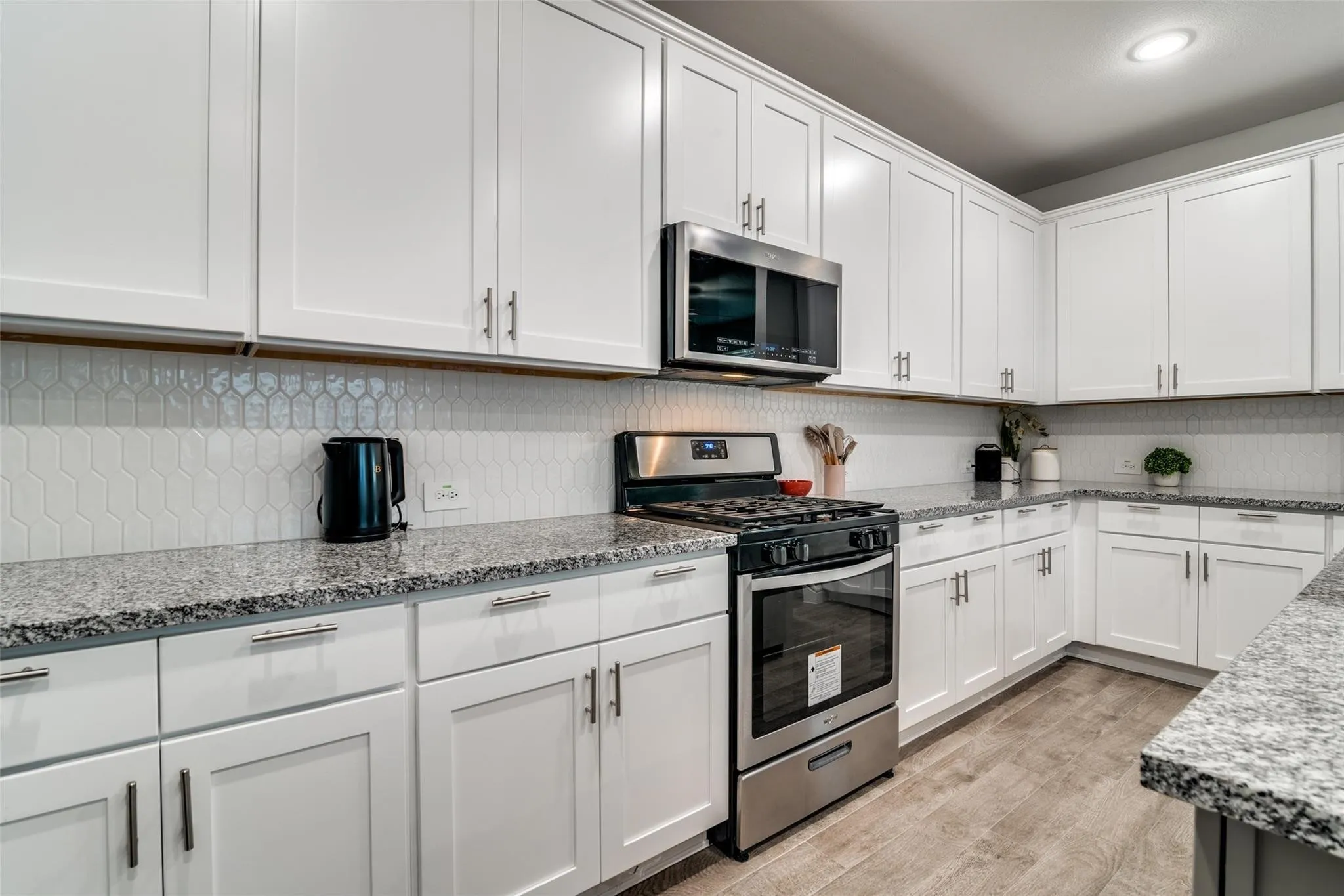 Kitchen with appliances with stainless steel finishes, light stone countertops, white cabinets, and light wood-type flooring