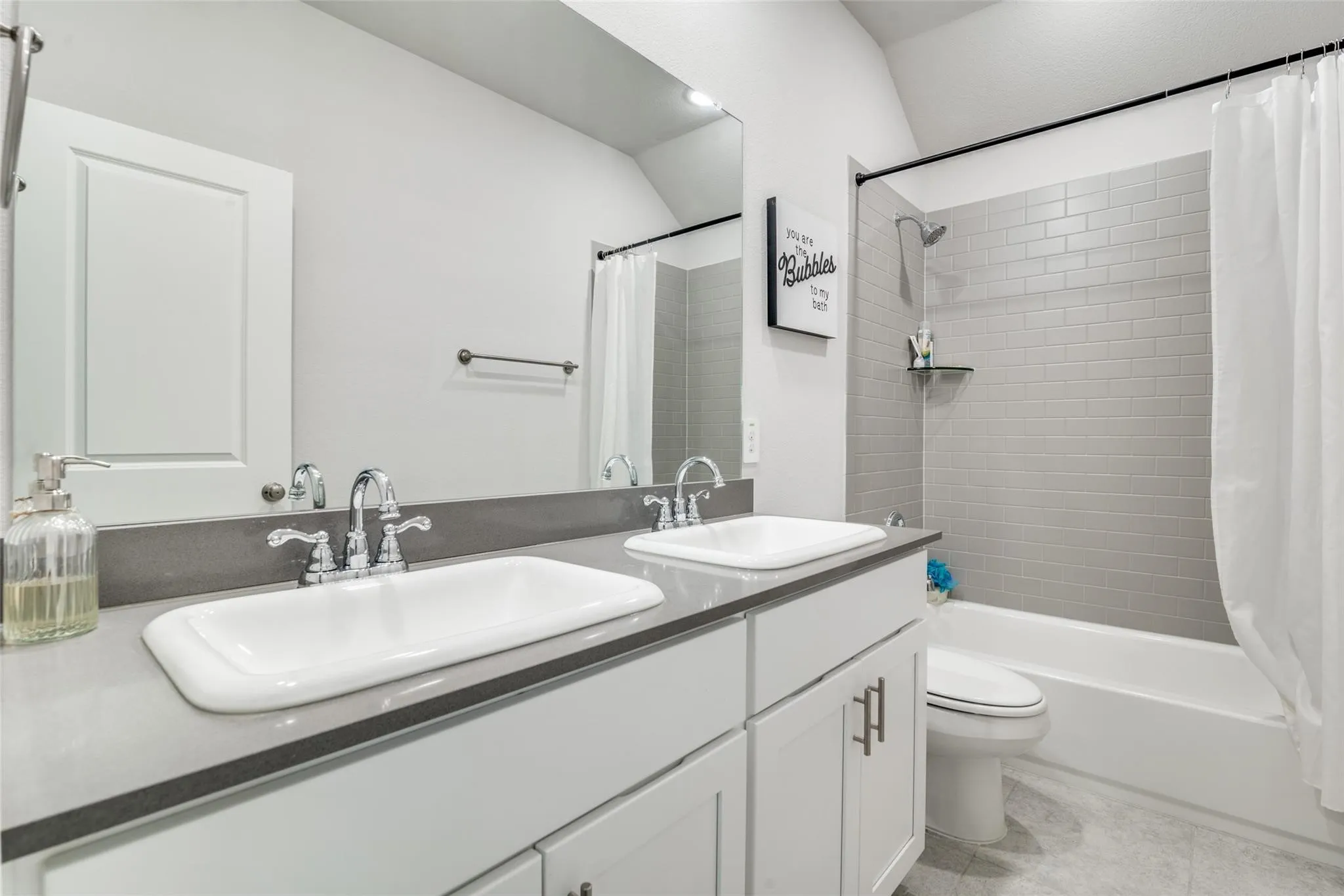 Full bath with double vanity, shower / tub combo, and light tile patterned floors