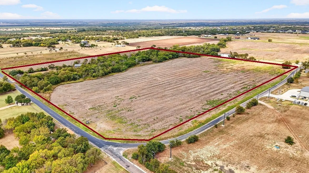 Expansive undeveloped land featuring a cleared field, mature tree lines, and paved road frontage