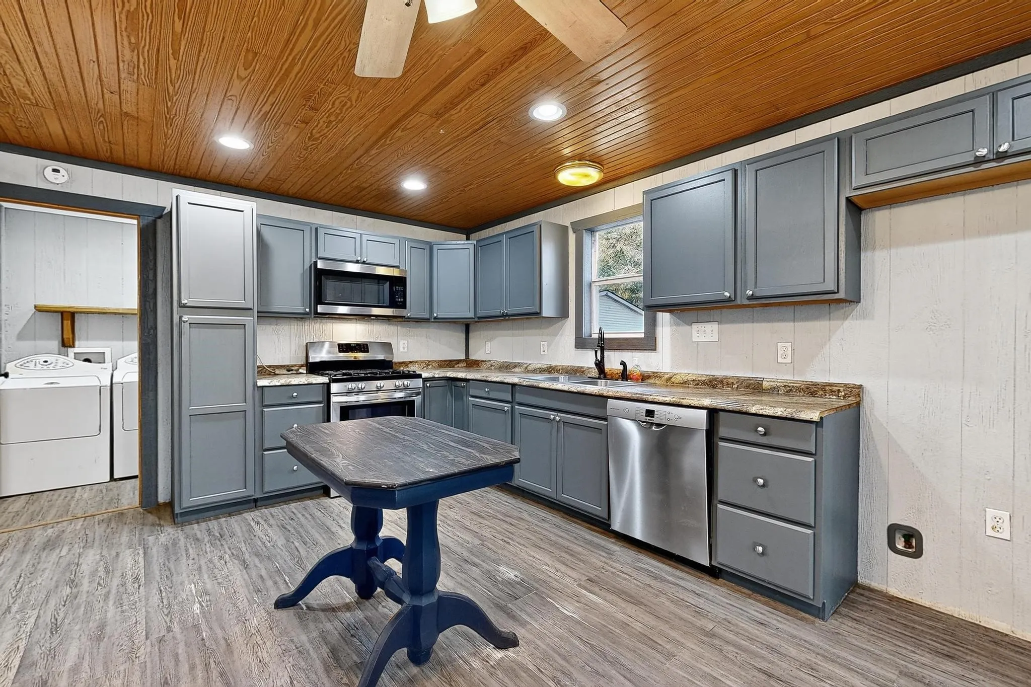 Kitchen with gray cabinetry, recessed lighting, light wood finished floors, wooden walls, and stainless steel appliances