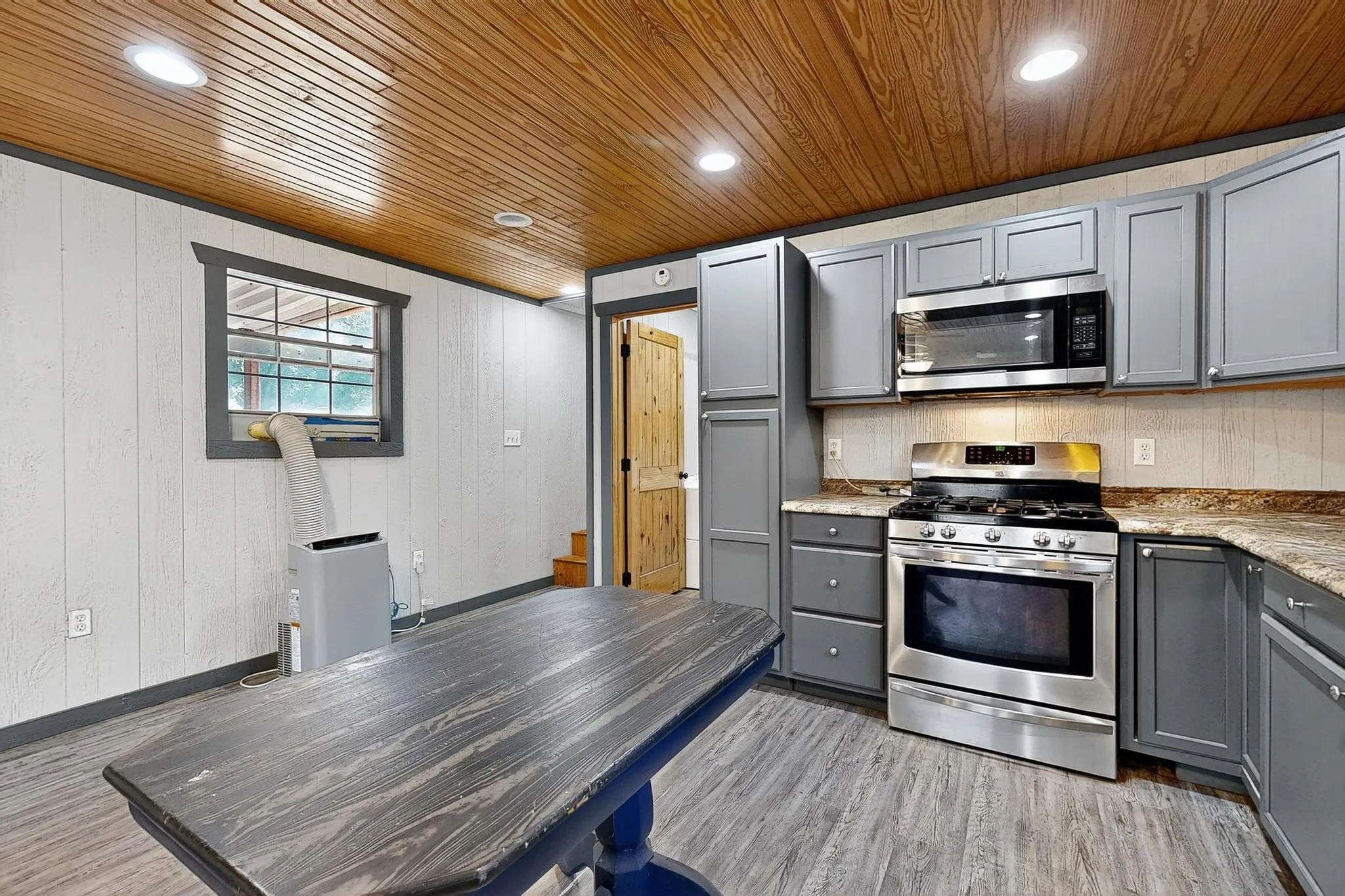 Kitchen featuring gray cabinets, stainless steel appliances, recessed lighting, wooden walls, and light wood-style floors