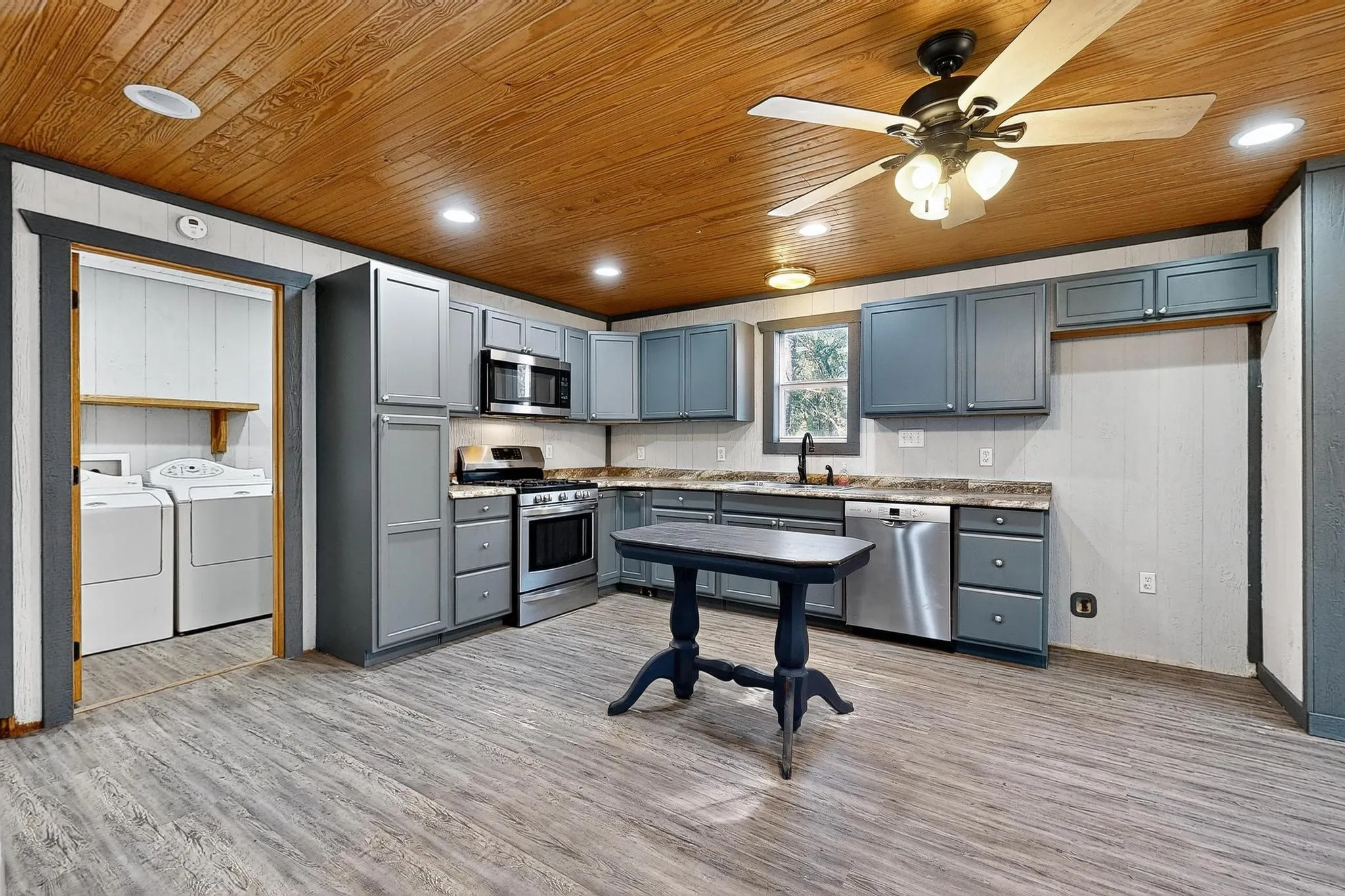 Kitchen with gray cabinetry, wood walls, light wood-type flooring, stainless steel appliances, and wood ceiling
