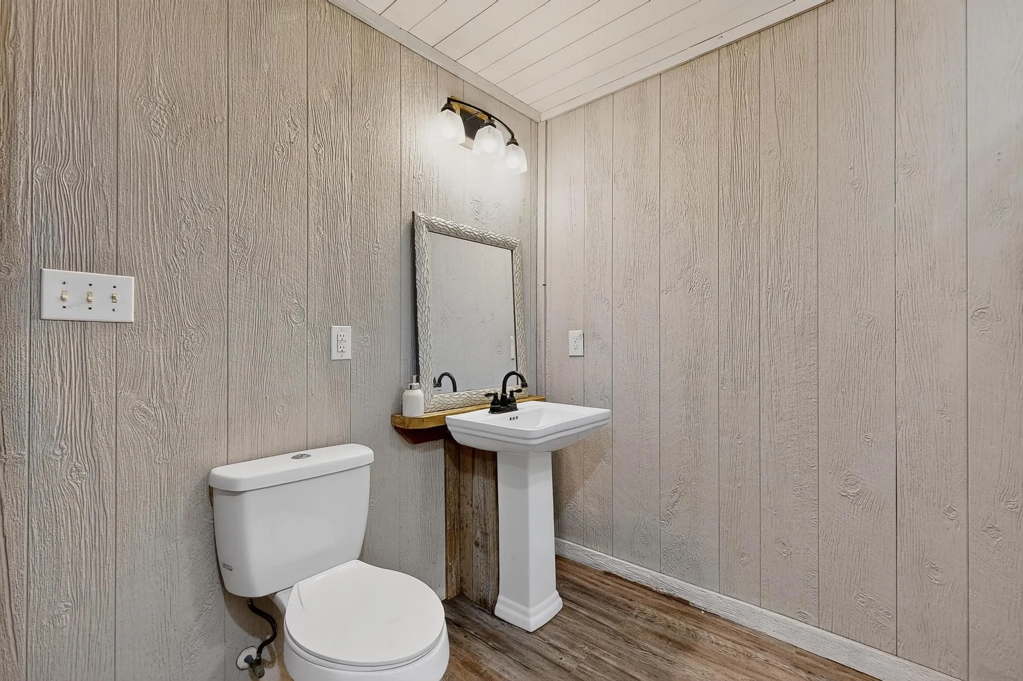 Half bathroom featuring wood finished floors and wood walls