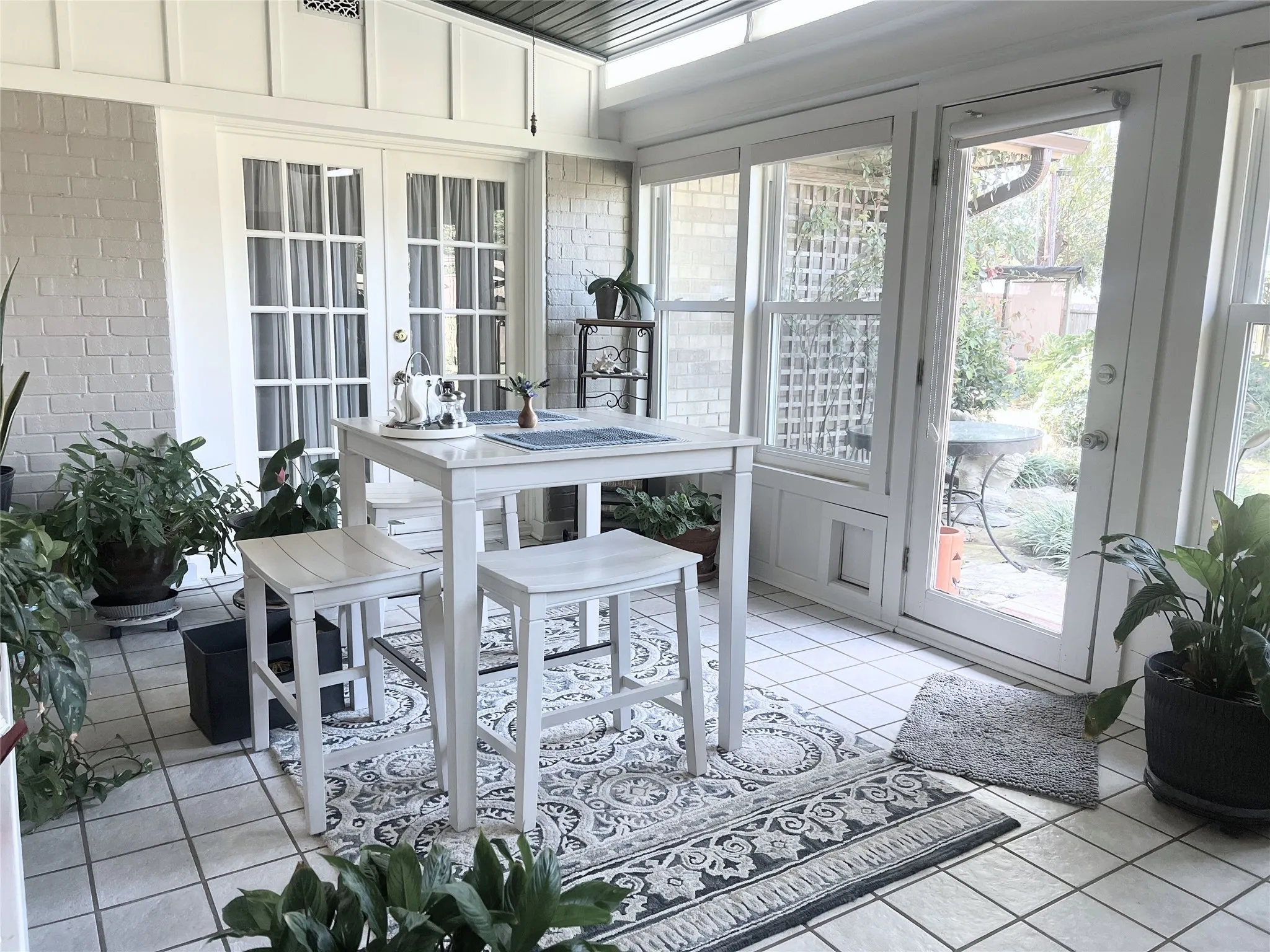 Sunroom with french doors, tile patterned floors, and brick wall