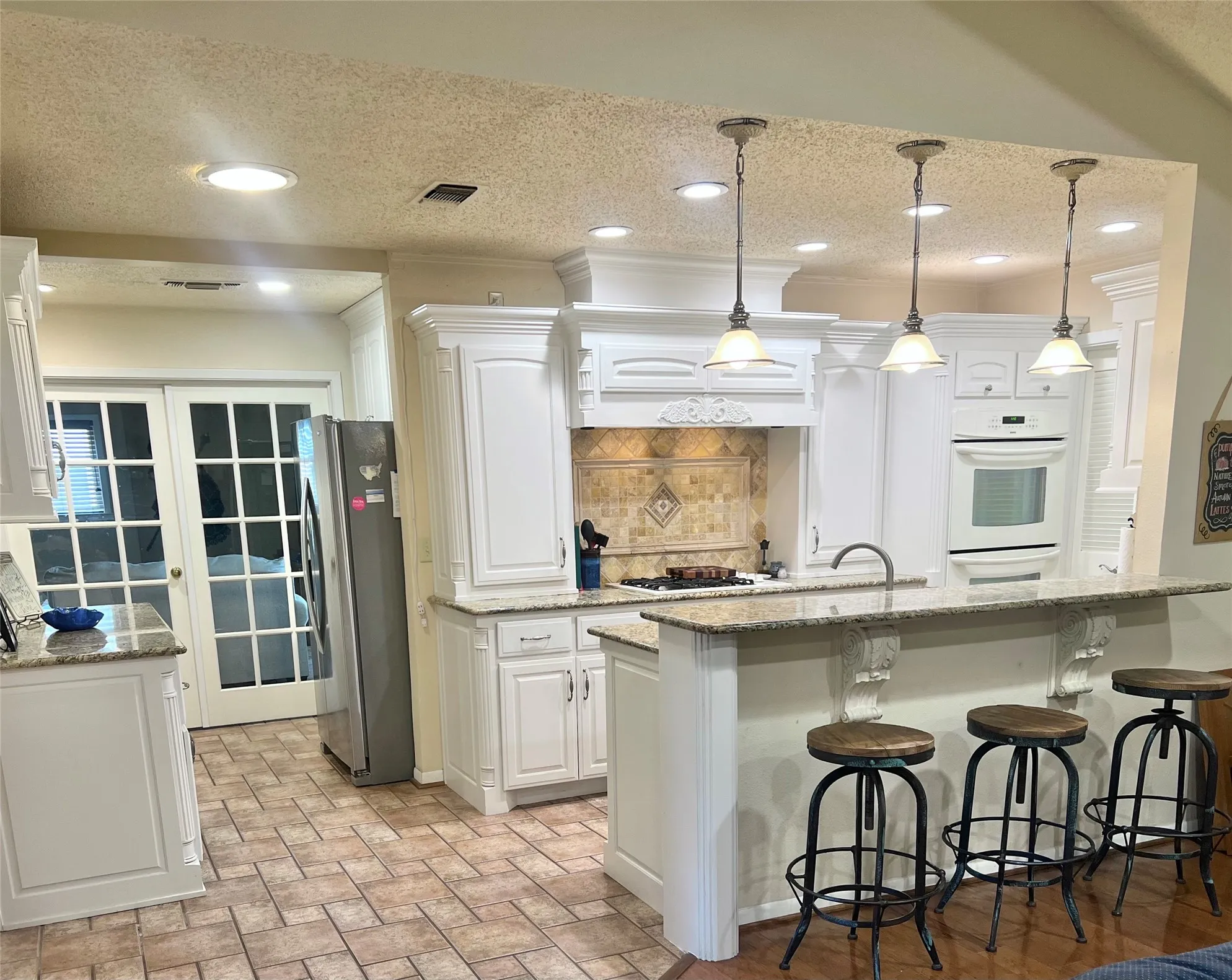Kitchen breakfast bar overlooks the Great room, tasteful backsplash, and pendant and recessed lighting.