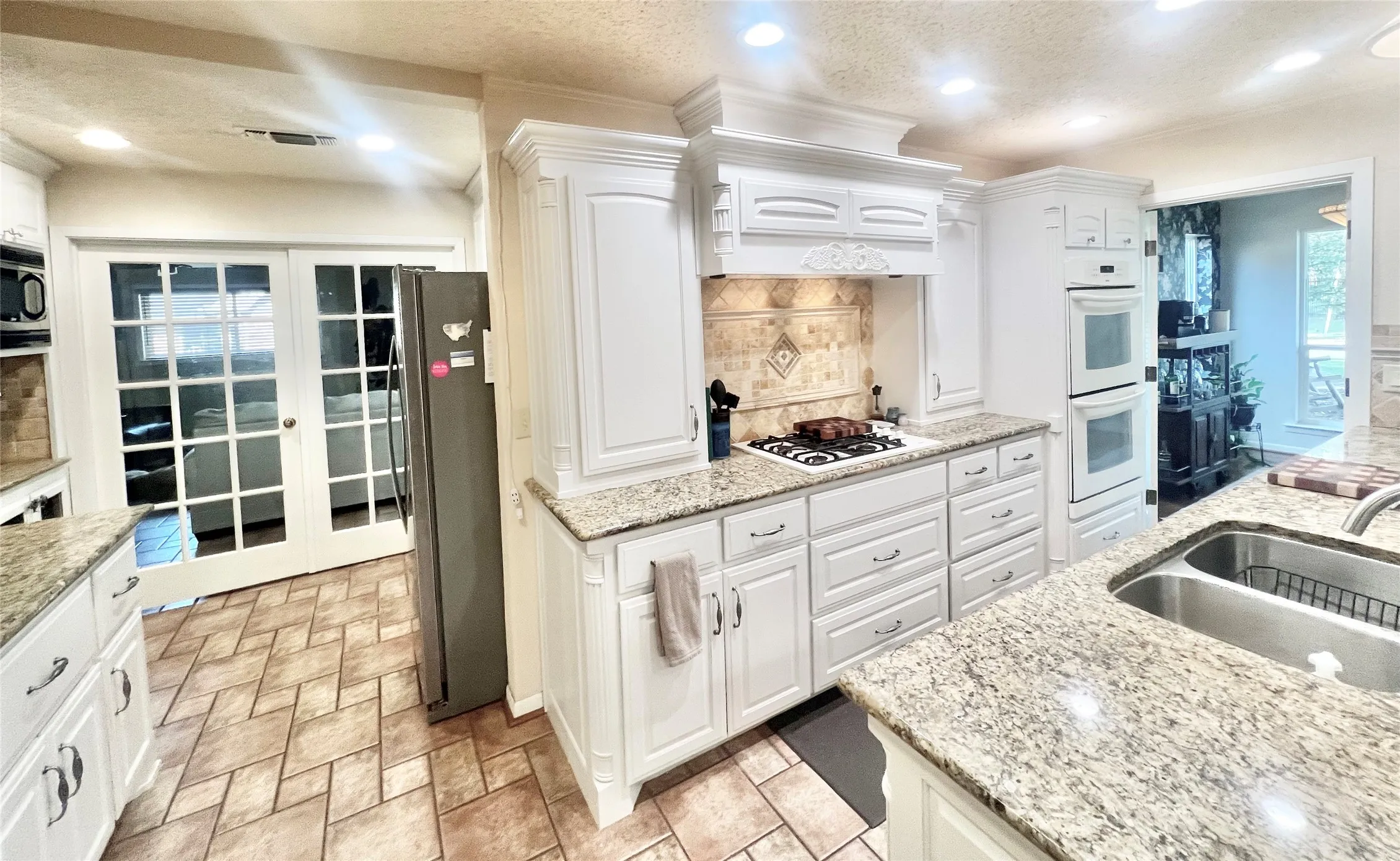Kitchen with white cabinets, gas cooktop, granite counters, double ovens, microwave, dishwasher and in an L shape, providing additional cabinets for storage.