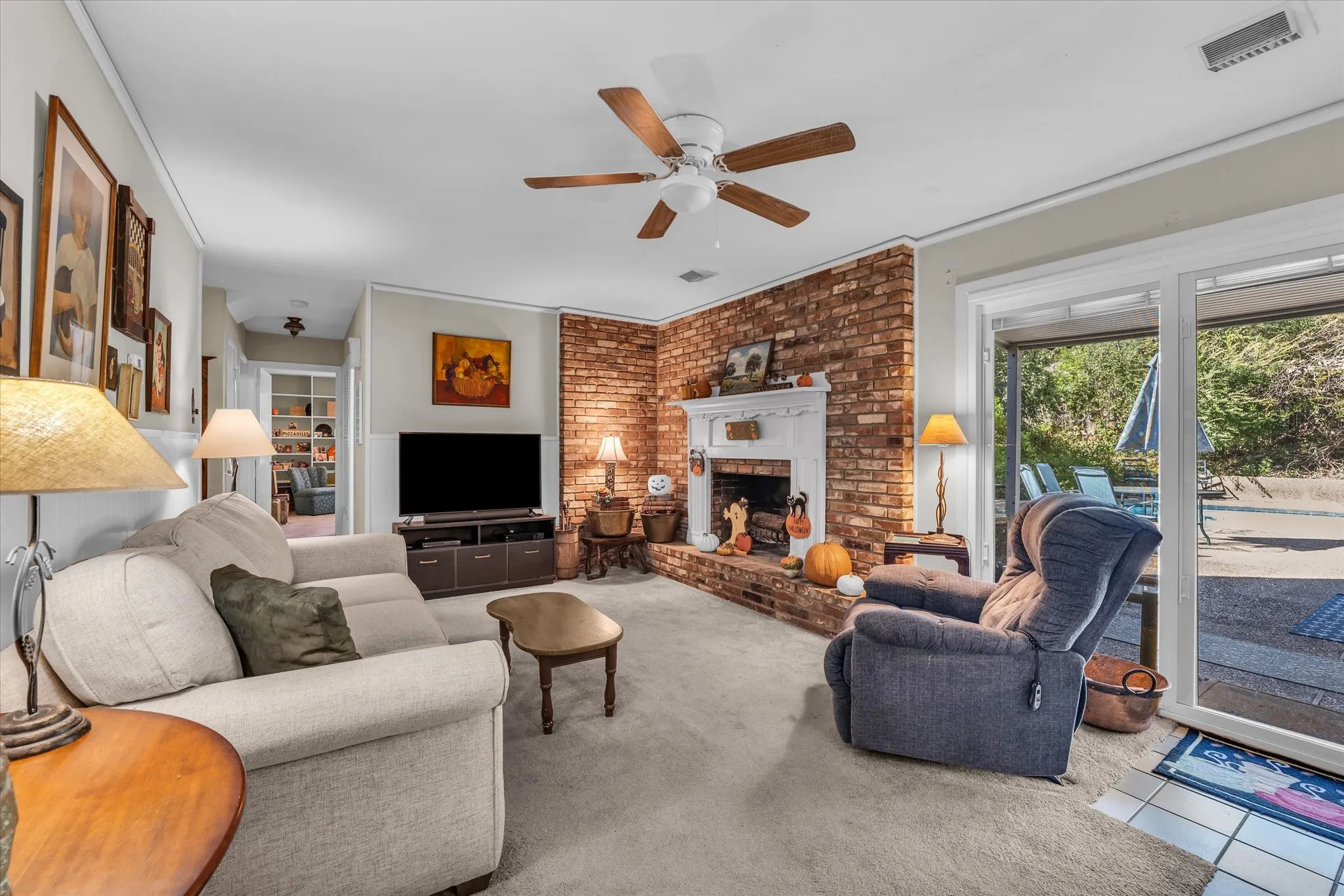 Carpeted living room with a brick fireplace and ceiling fan