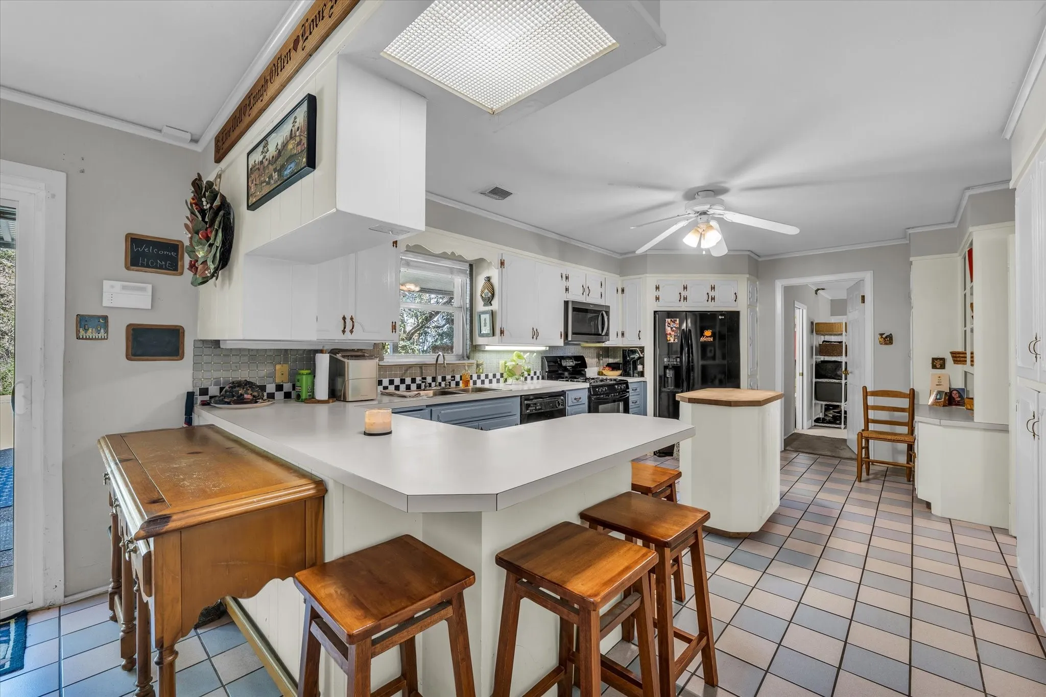 Kitchen featuring light tile patterned floors, light countertops, a kitchen bar, crown molding, and a peninsula