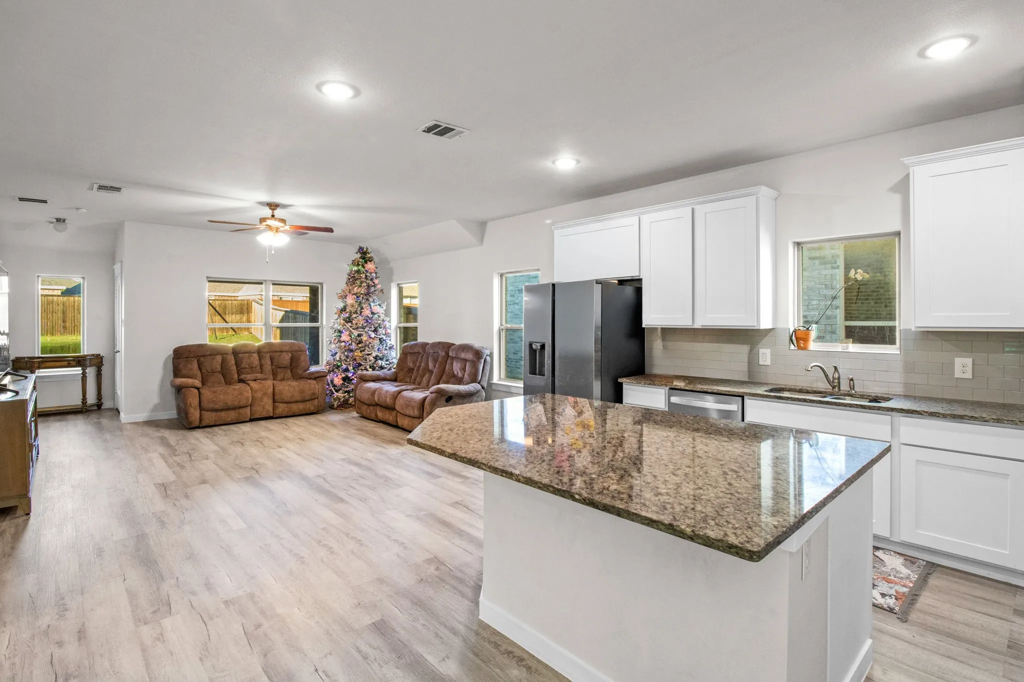 Kitchen with dark stone countertops, decorative backsplash, white cabinets, open floor plan, and recessed lighting