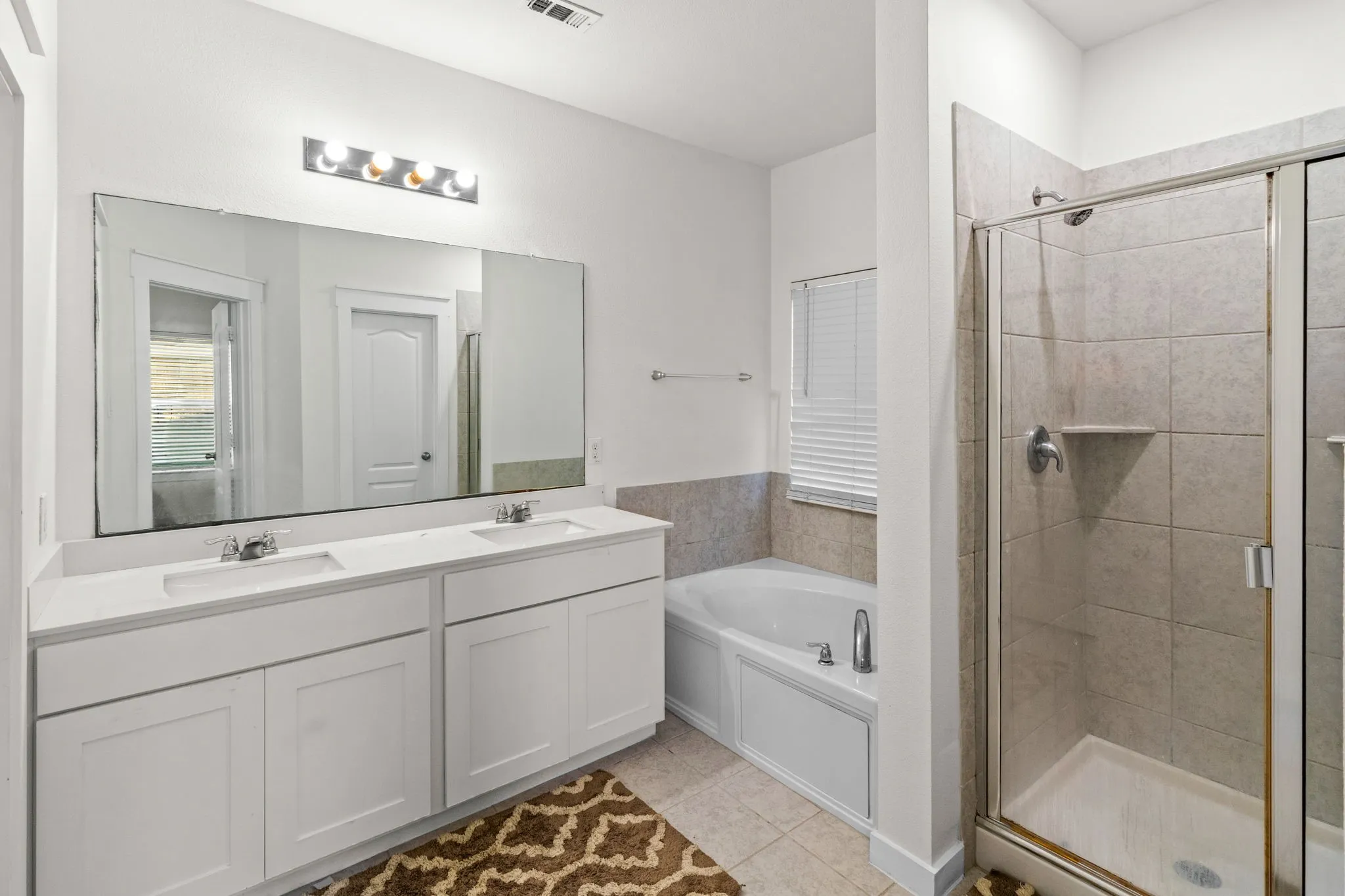 Bathroom featuring a bath, a shower stall, double vanity, and light tile patterned flooring