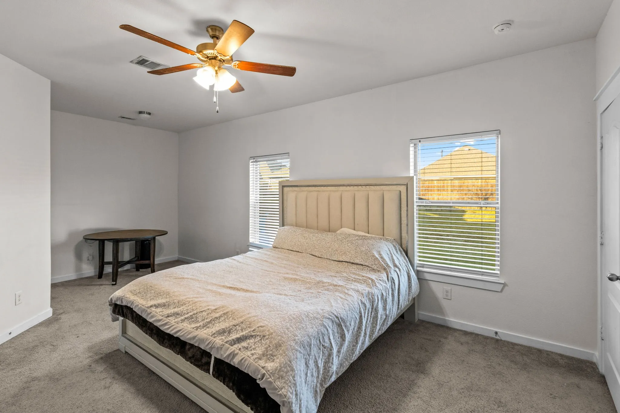 Bedroom with light carpet, multiple windows, and ceiling fan
