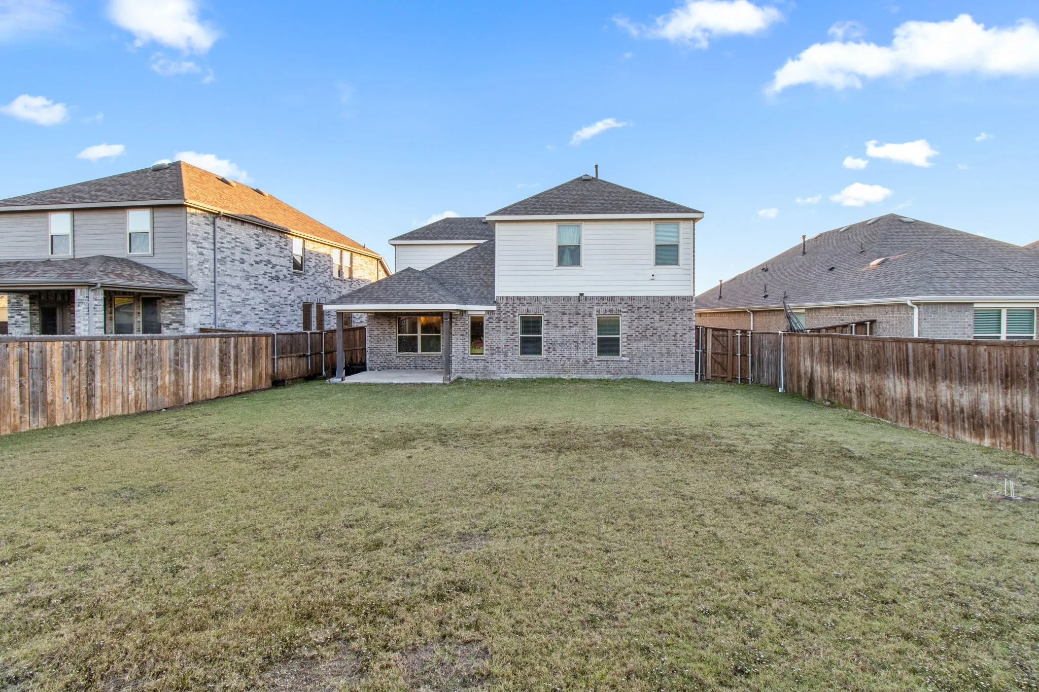 Rear view of house with a patio, brick siding, a fenced backyard, and roof with shingles