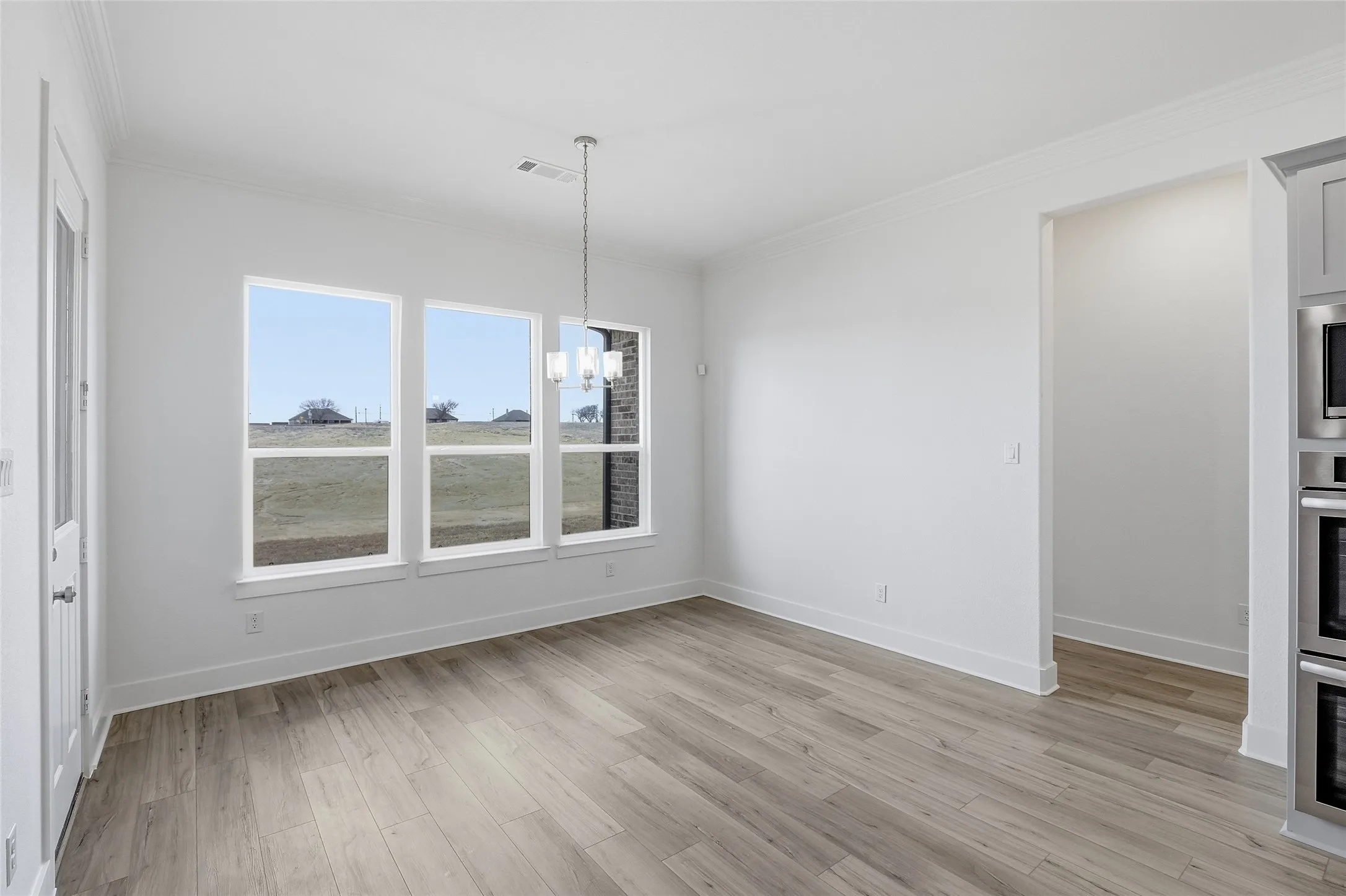 Unfurnished dining area with suspended lighting, crown molding, and light wood-type flooring