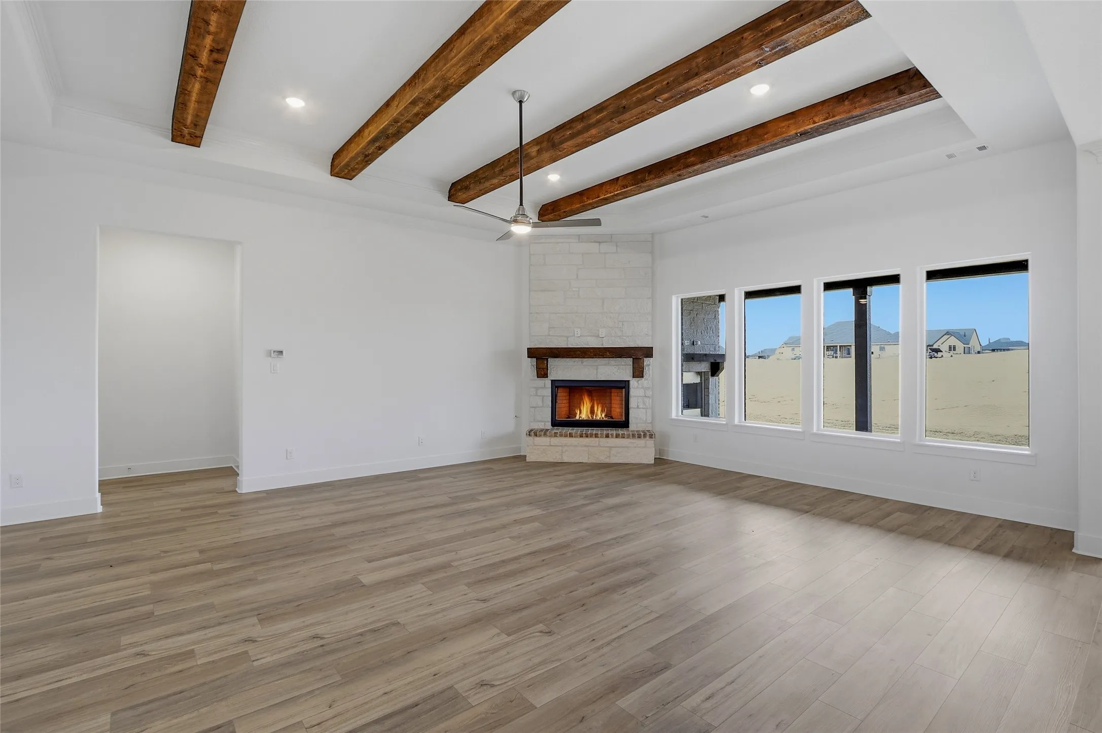 Unfurnished living room featuring a stone fireplace, recessed lighting, light wood-style flooring, a ceiling fan, and beam ceiling