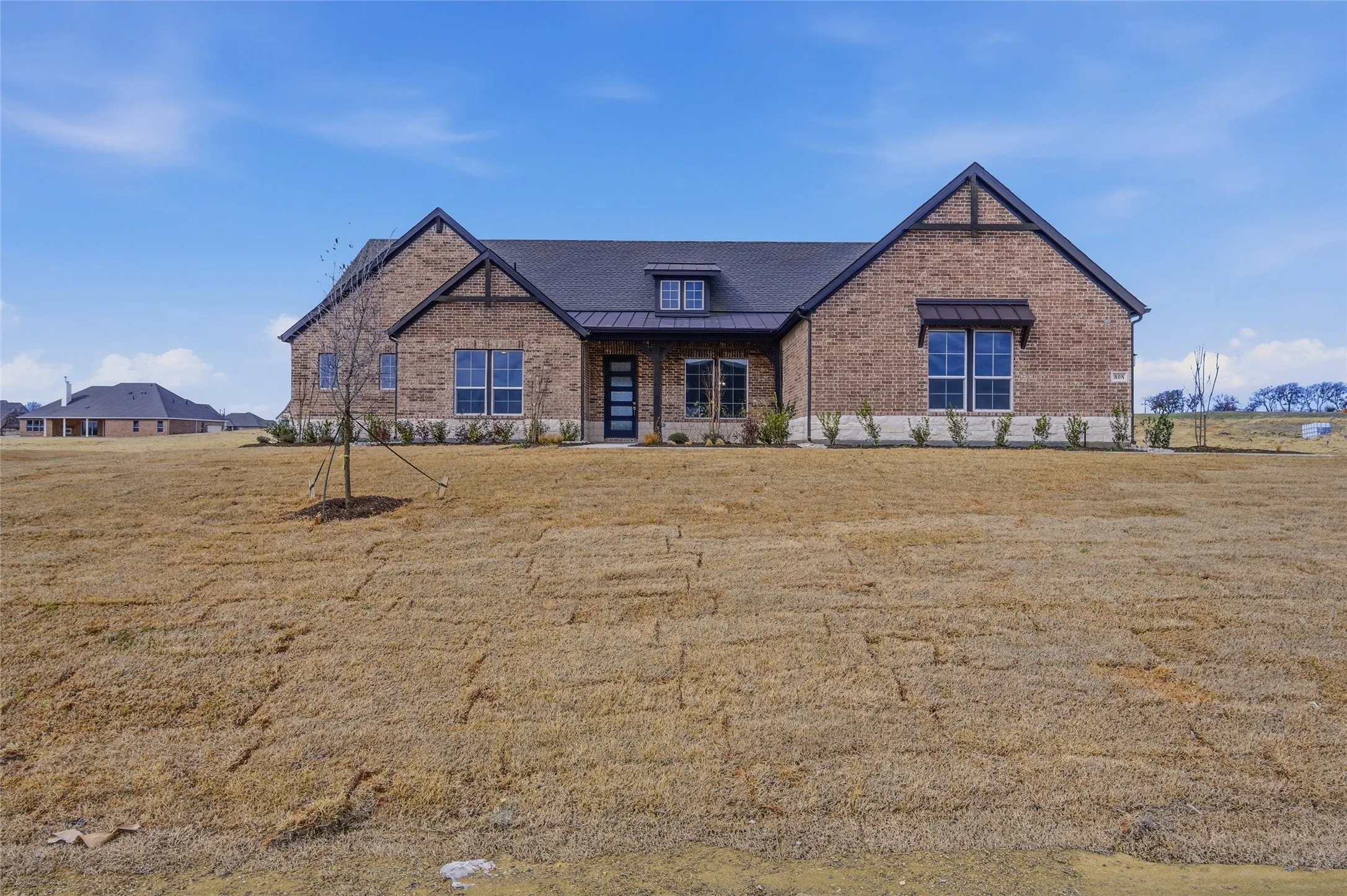 View of front facade with a standing seam roof, brick siding, and a front yard