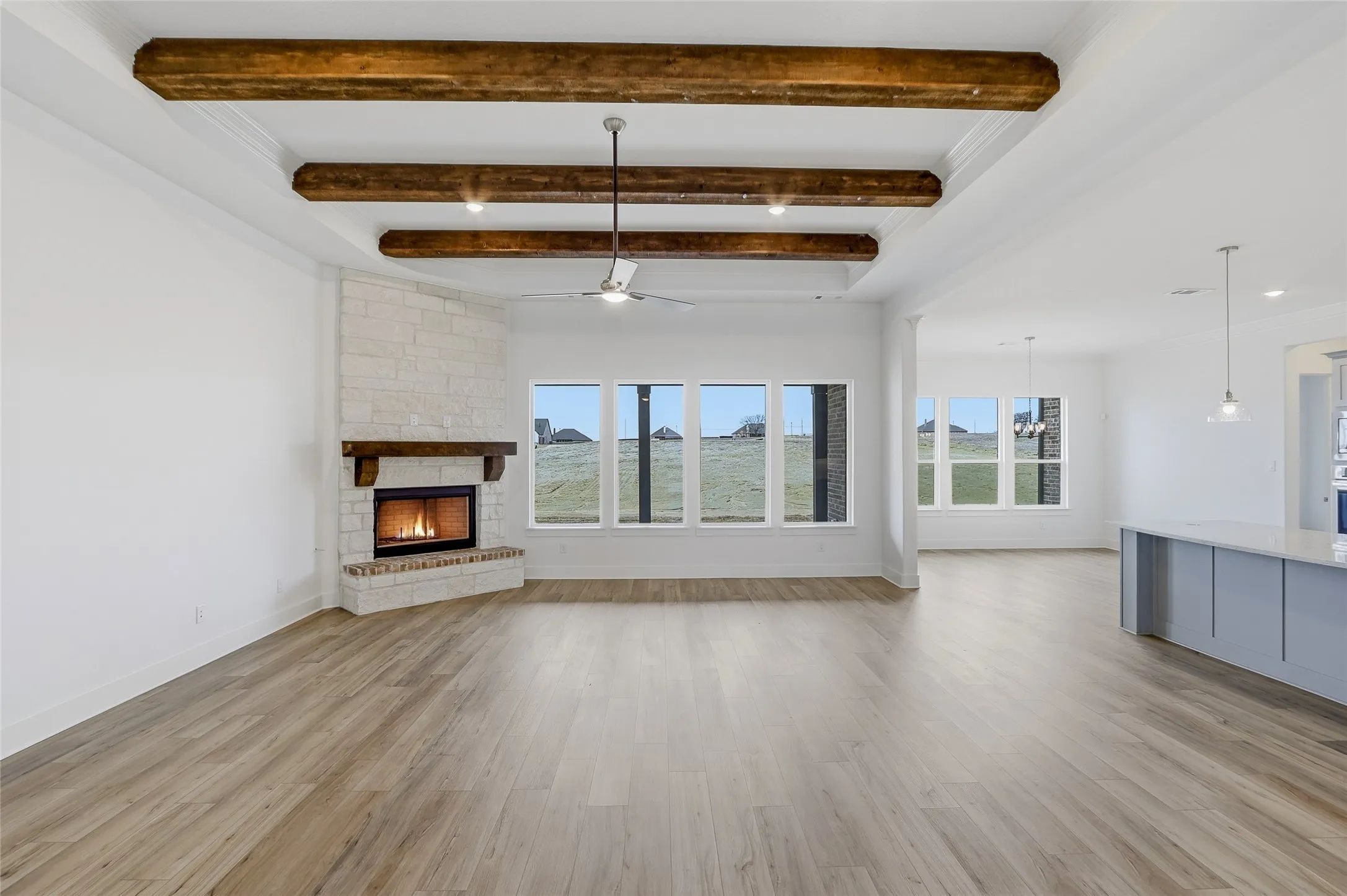 Unfurnished living room with a stone fireplace, a ceiling fan, light wood-type flooring, beamed ceiling, and ornamental molding