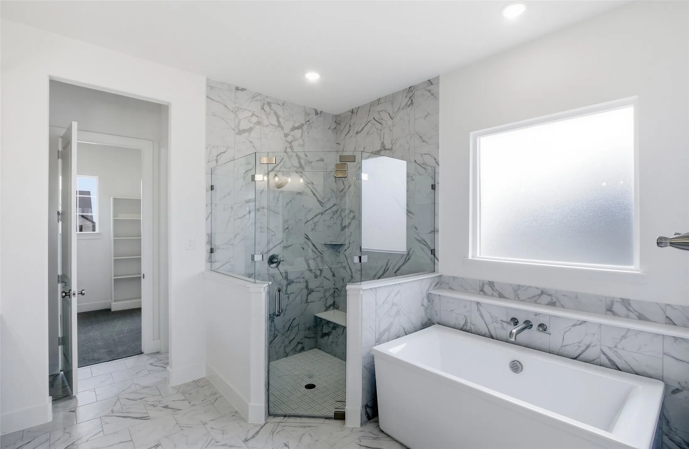 Bathroom featuring light marble finish floors, healthy amount of natural light, a spacious closet, a soaking tub, and recessed lighting