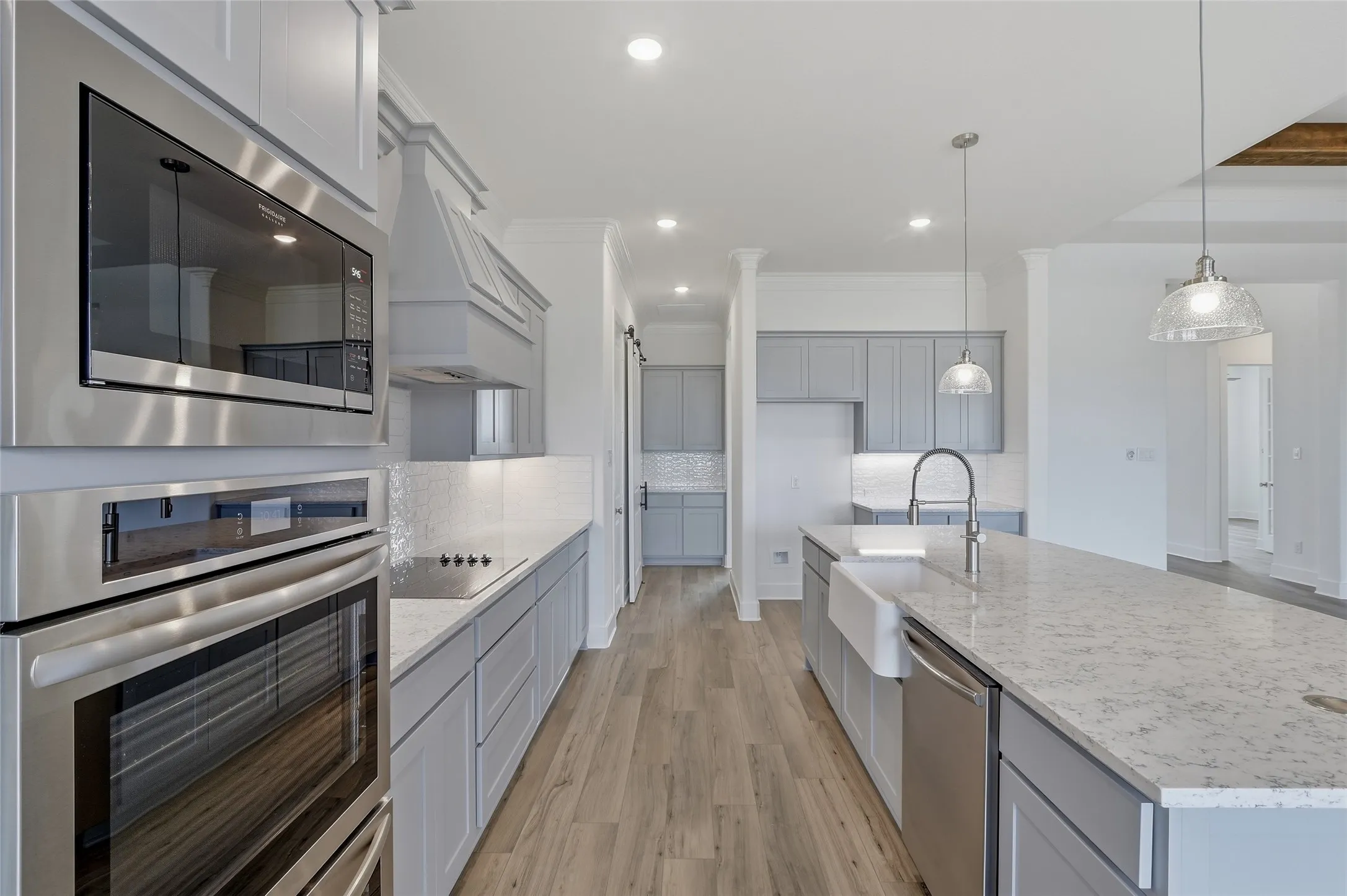 Kitchen with stainless steel appliances, gray cabinets, light wood-style flooring, light stone countertops, and ornamental molding