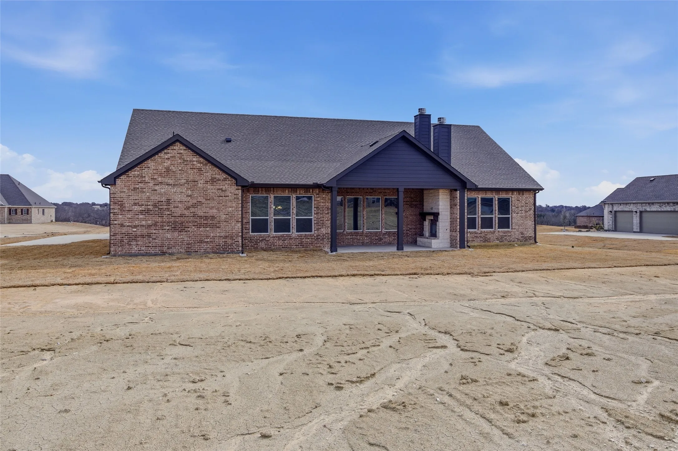 Craftsman-style house featuring a patio area, a chimney, brick siding, and a shingled roof