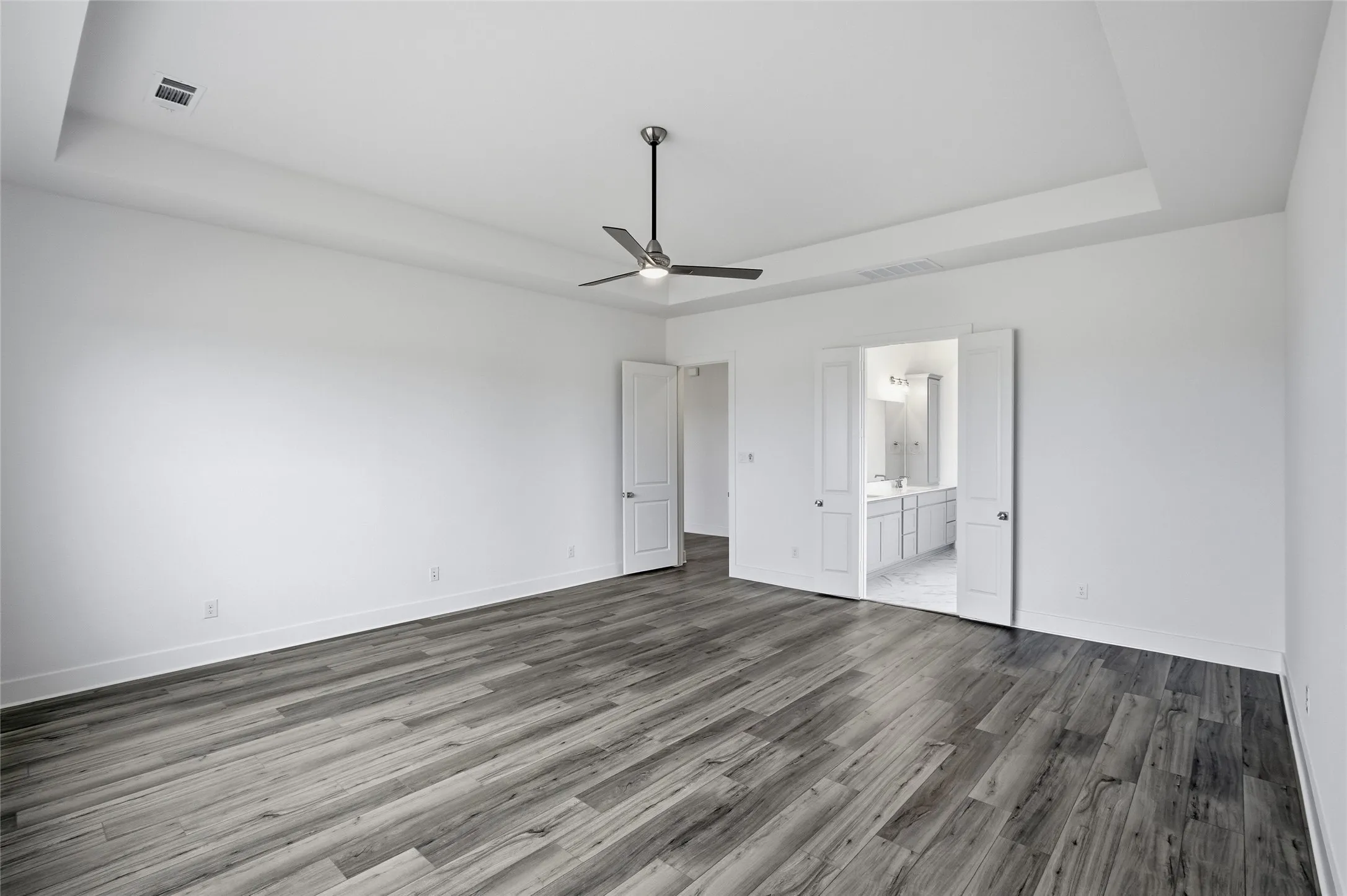 Unfurnished bedroom featuring a tray ceiling, ceiling fan, wood finished floors, and connected bathroom