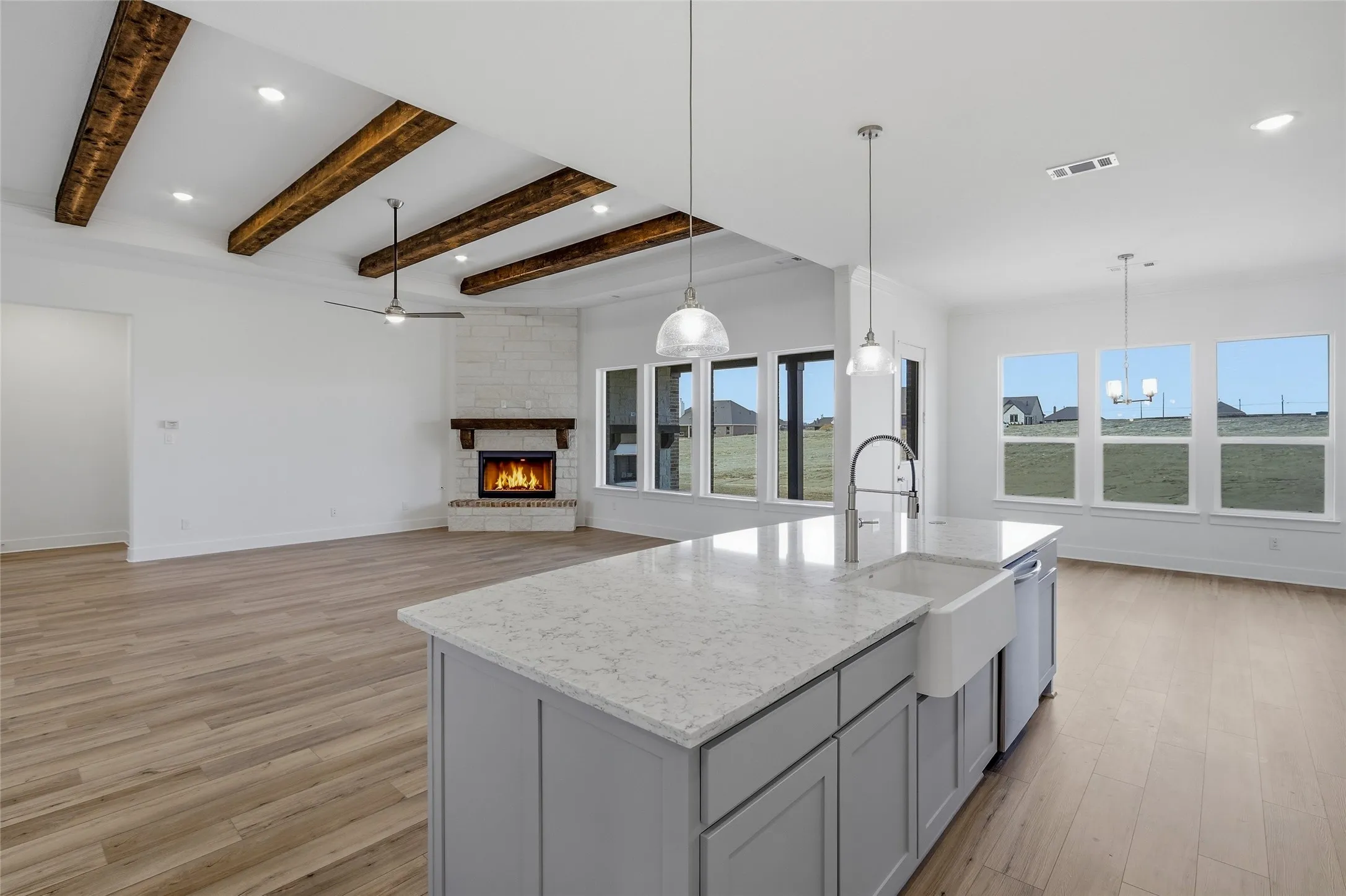 Kitchen with a fireplace, gray cabinetry, pendant lighting, light wood-style floors, and beam ceiling