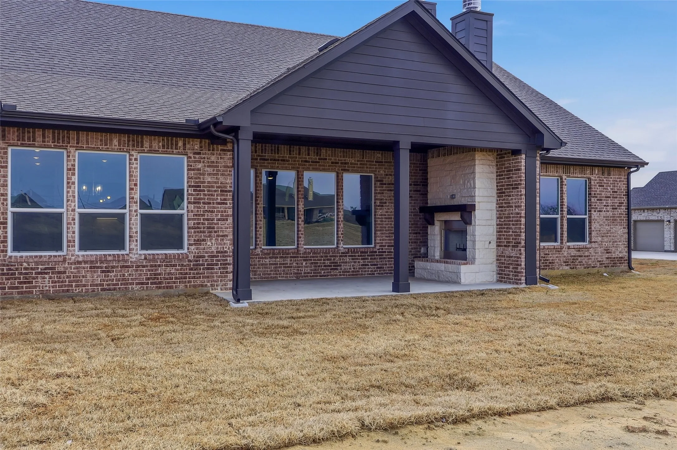 Rear view of property featuring brick siding, a lawn, a patio, a chimney, and a shingled roof